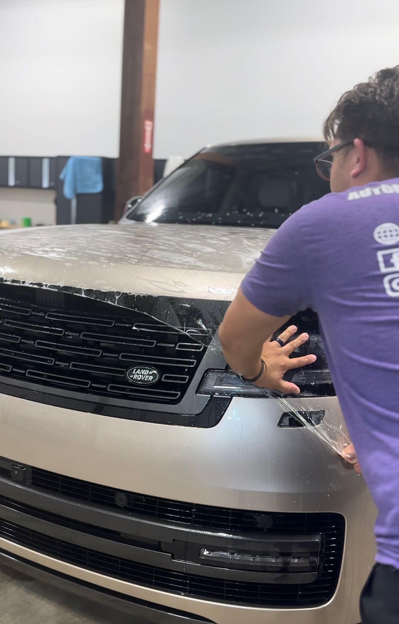 Person applying protective film to the headlight of a tan Land Rover SUV in a garage.