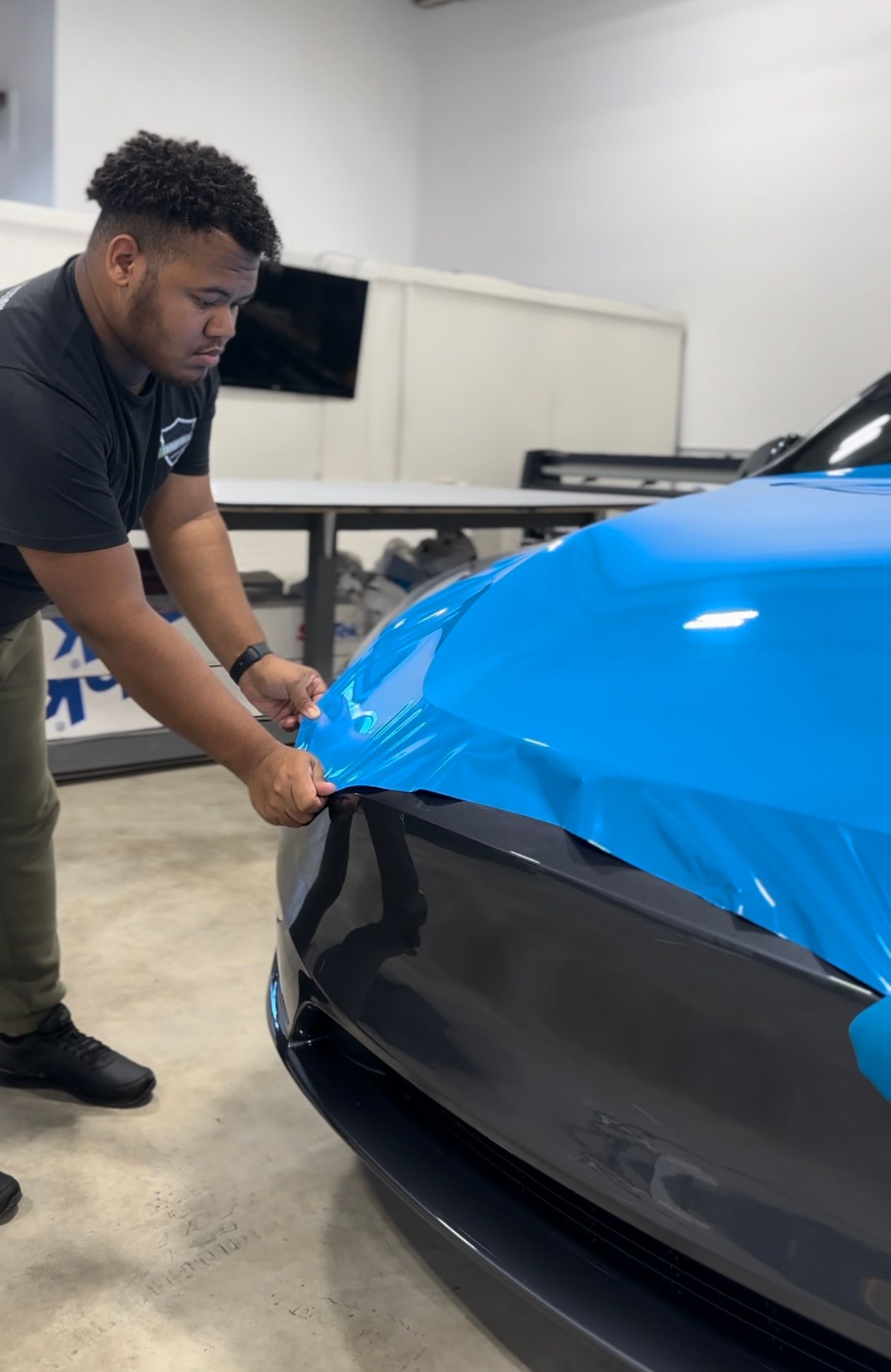a man is wrapping a blue car in a garage .