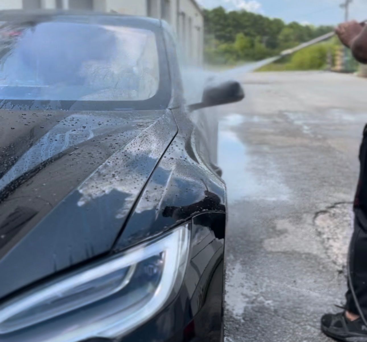 a man is washing a black car with a high pressure washer .
