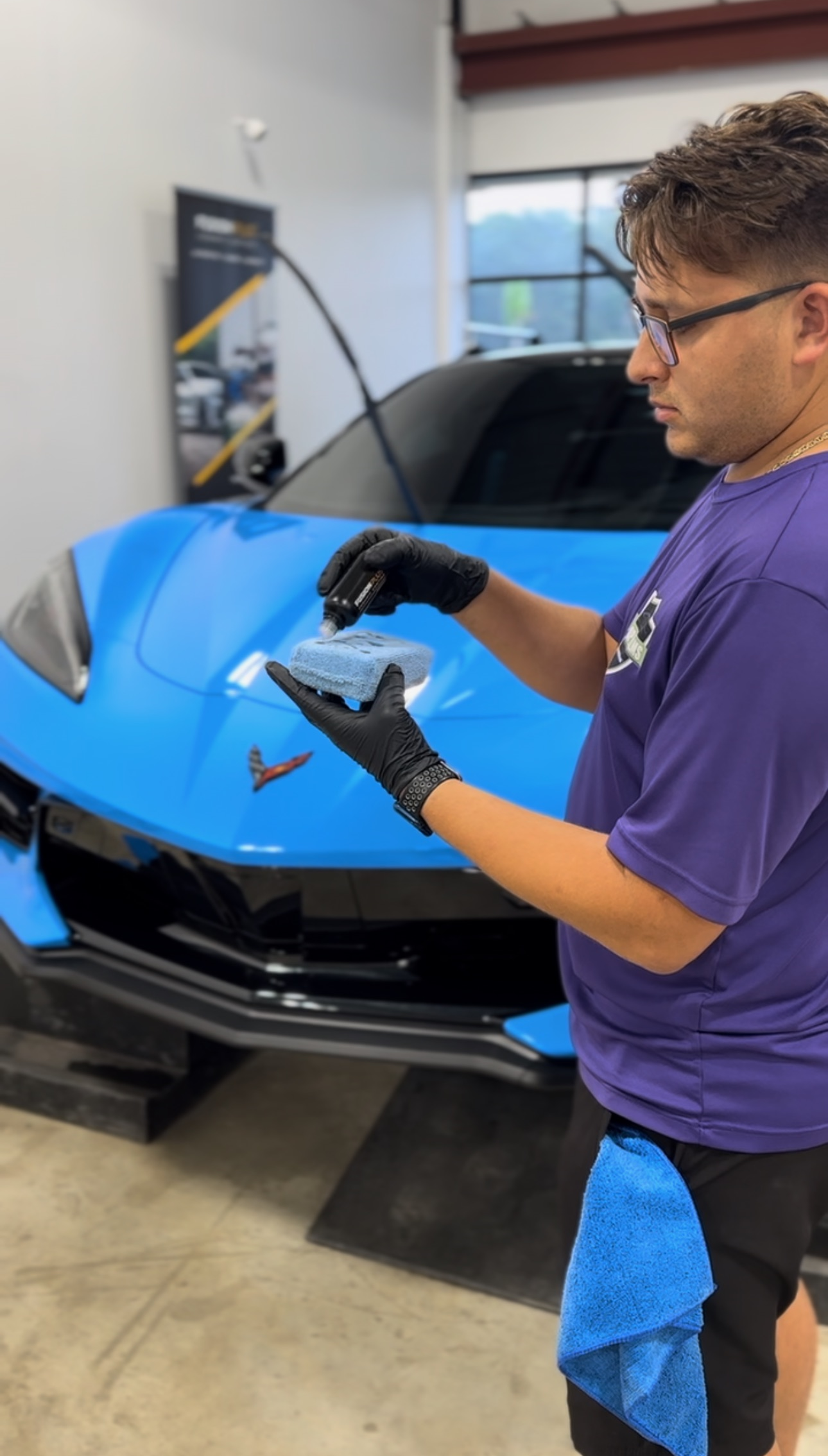 a man in a purple shirt is cleaning a blue car