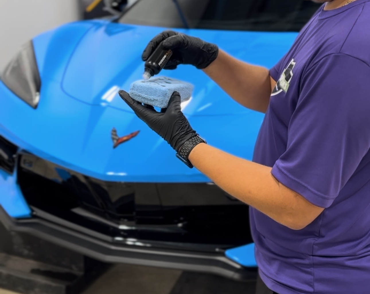 a man in a purple shirt is cleaning a blue car