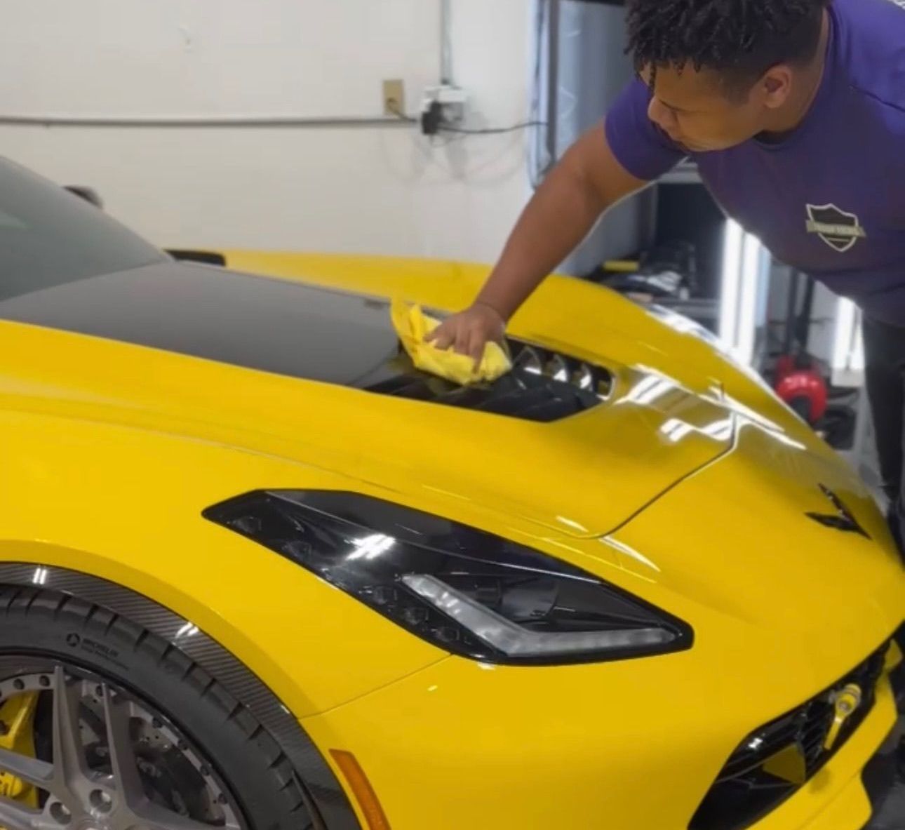 a man in a purple shirt is cleaning a yellow sports car