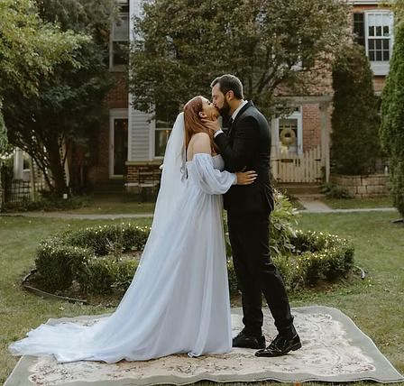 Couple kissing on a rug in a garden; woman in a white wedding dress, man in a black suit.