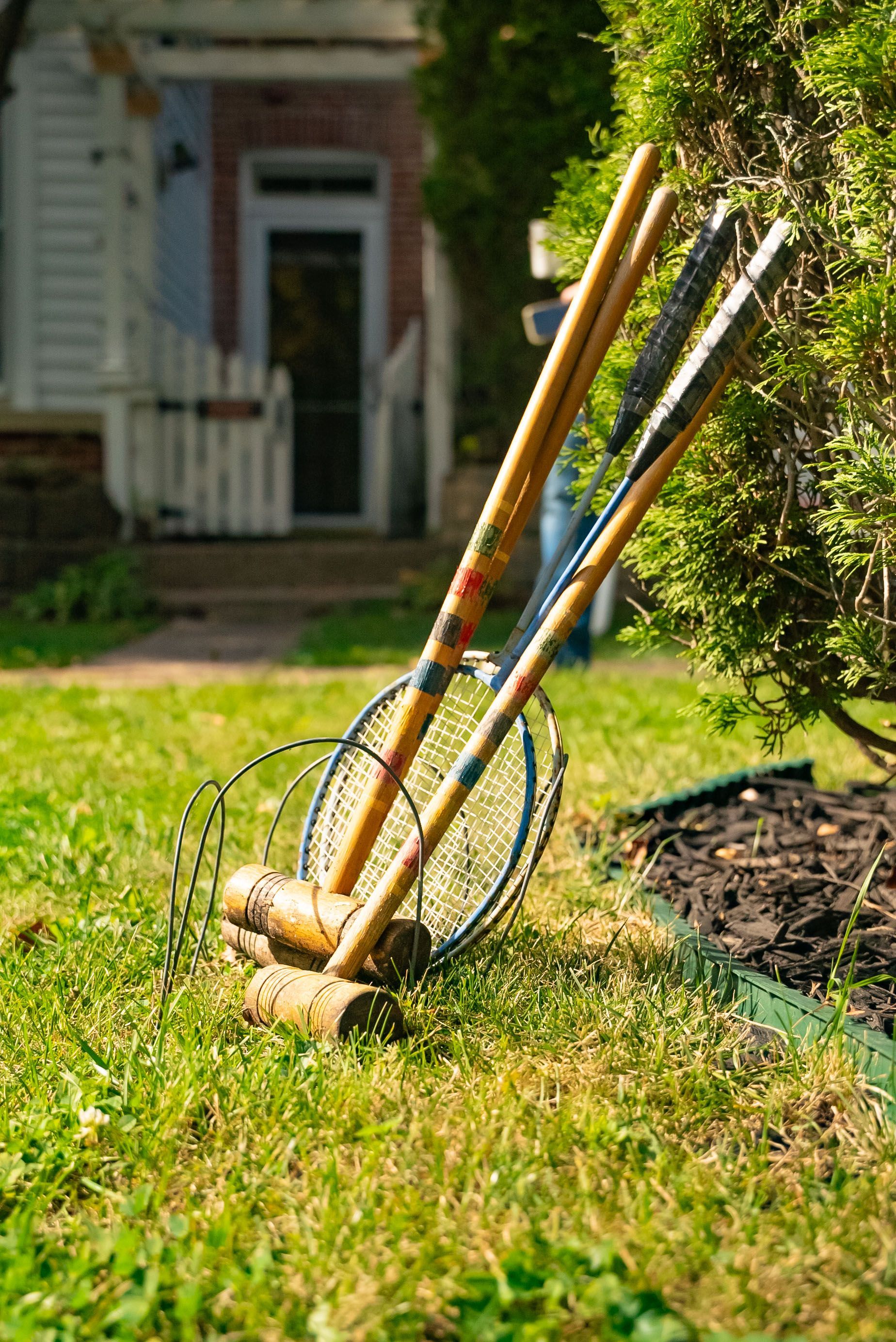Croquet mallets and hoops on a grassy lawn, with a house in the blurred background.