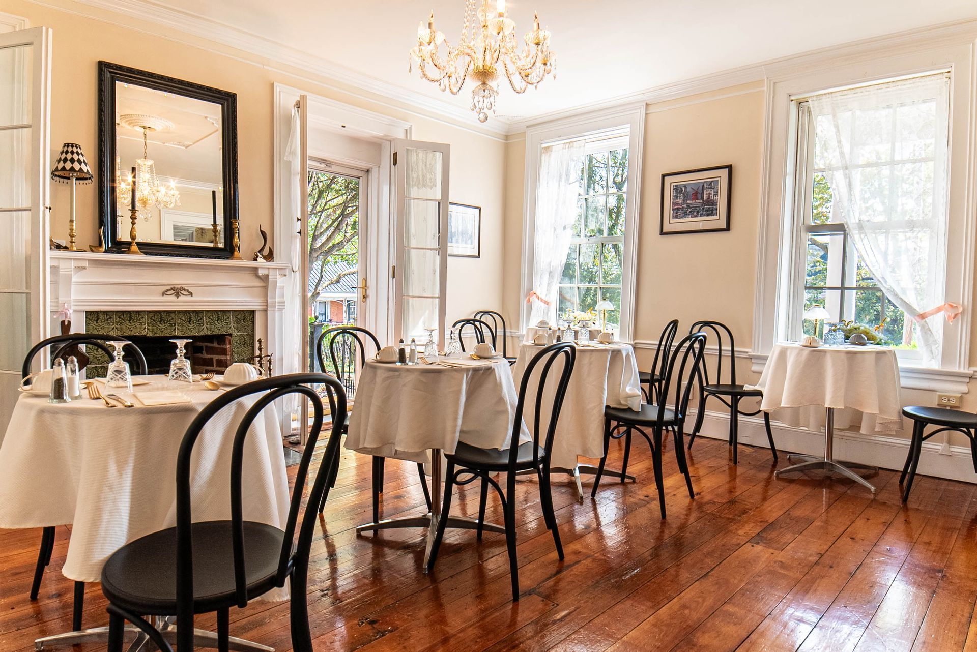 Dining room with round tables, white tablecloths, black chairs, and a chandelier.
