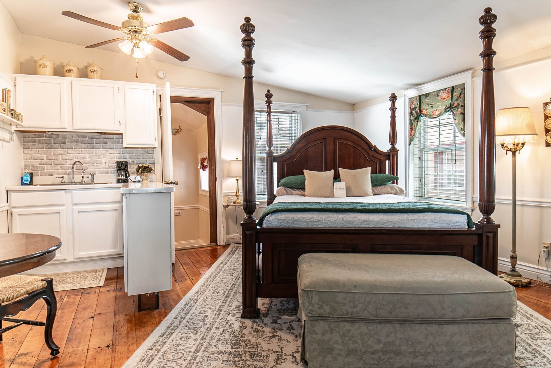 Bedroom with a four-poster bed, kitchenette, and rug on a hardwood floor.