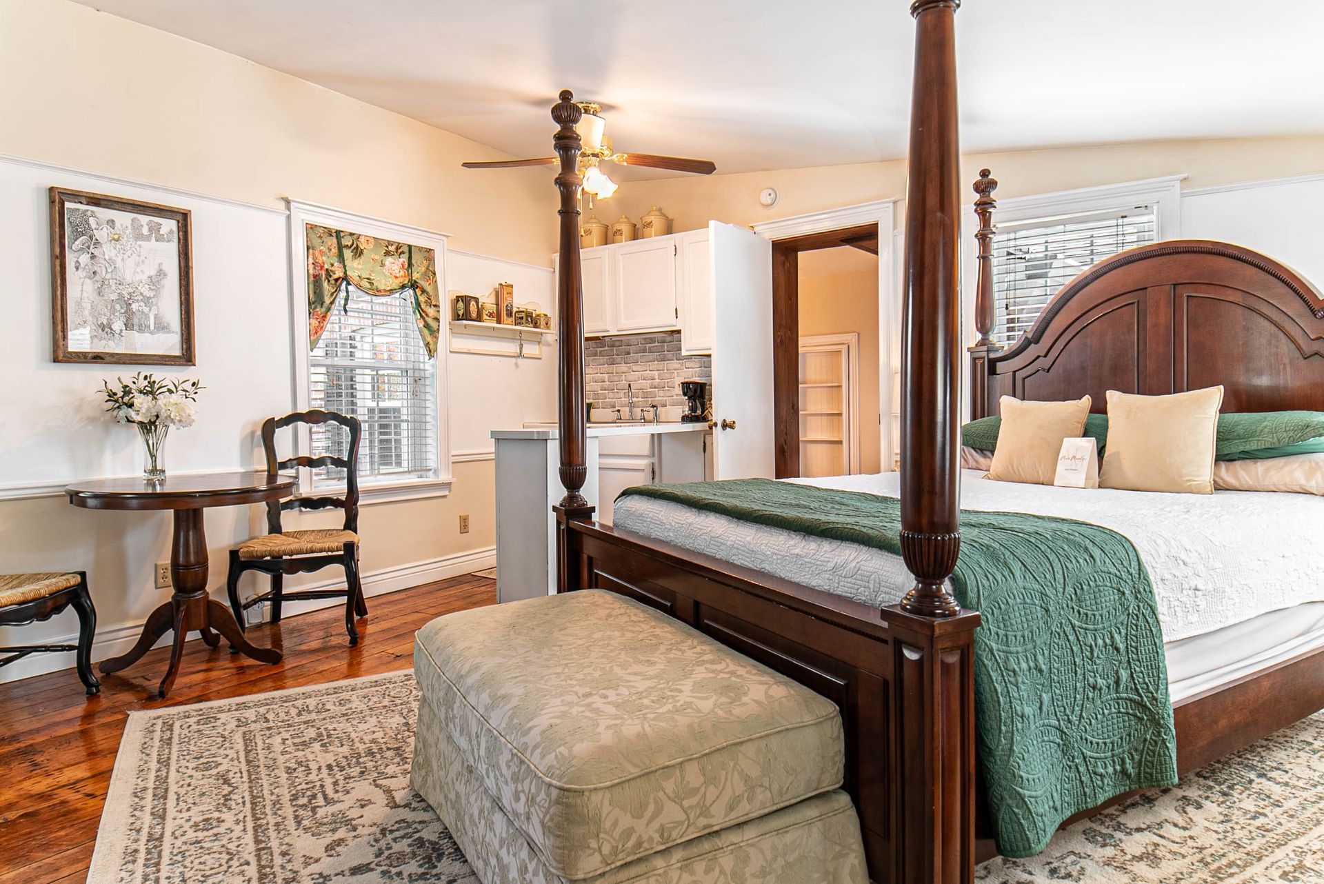 Bedroom with four-poster bed, small table and chairs, window with curtain, and small kitchenette.