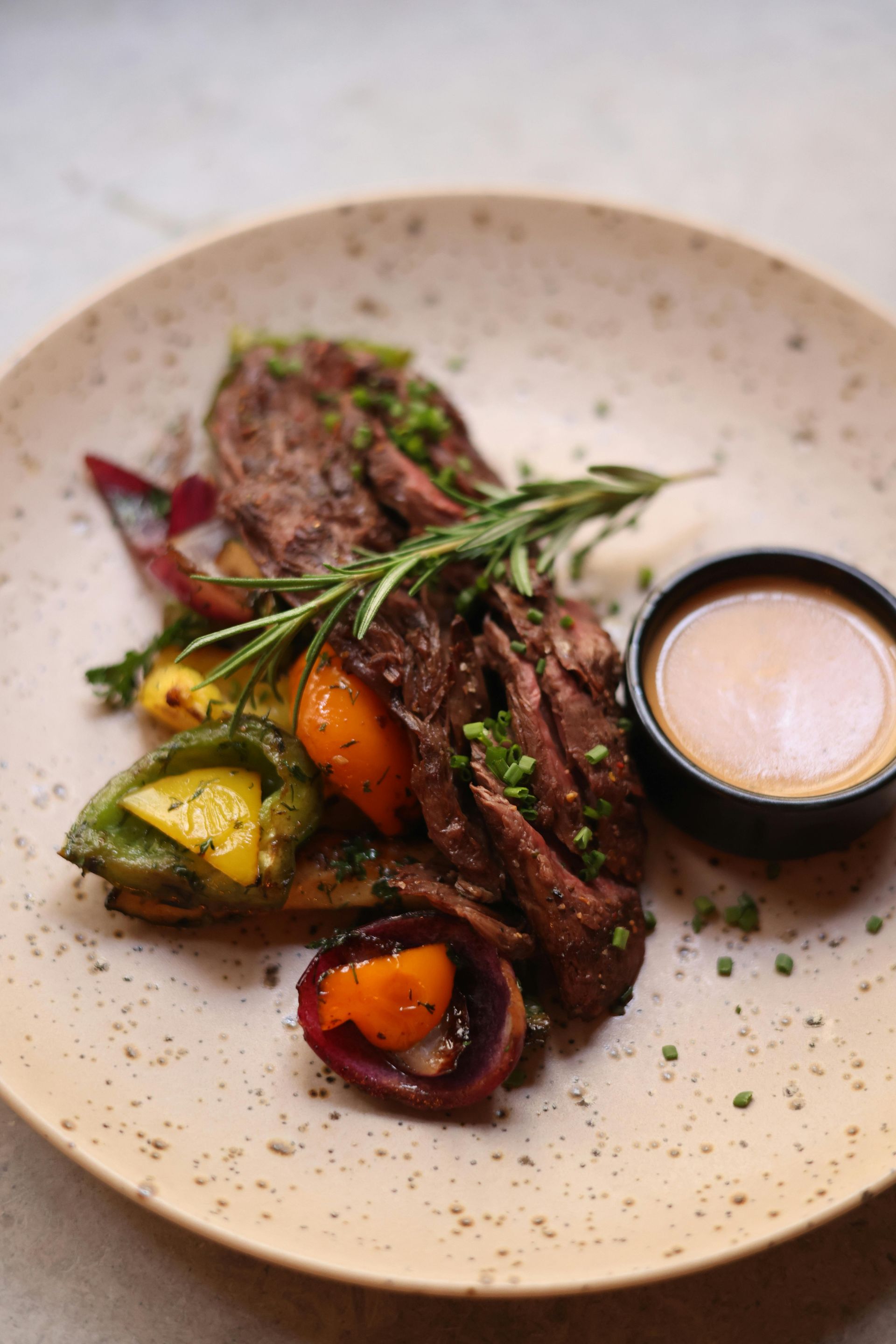 Grilled steak slices with roasted vegetables and sauce, garnished with rosemary.