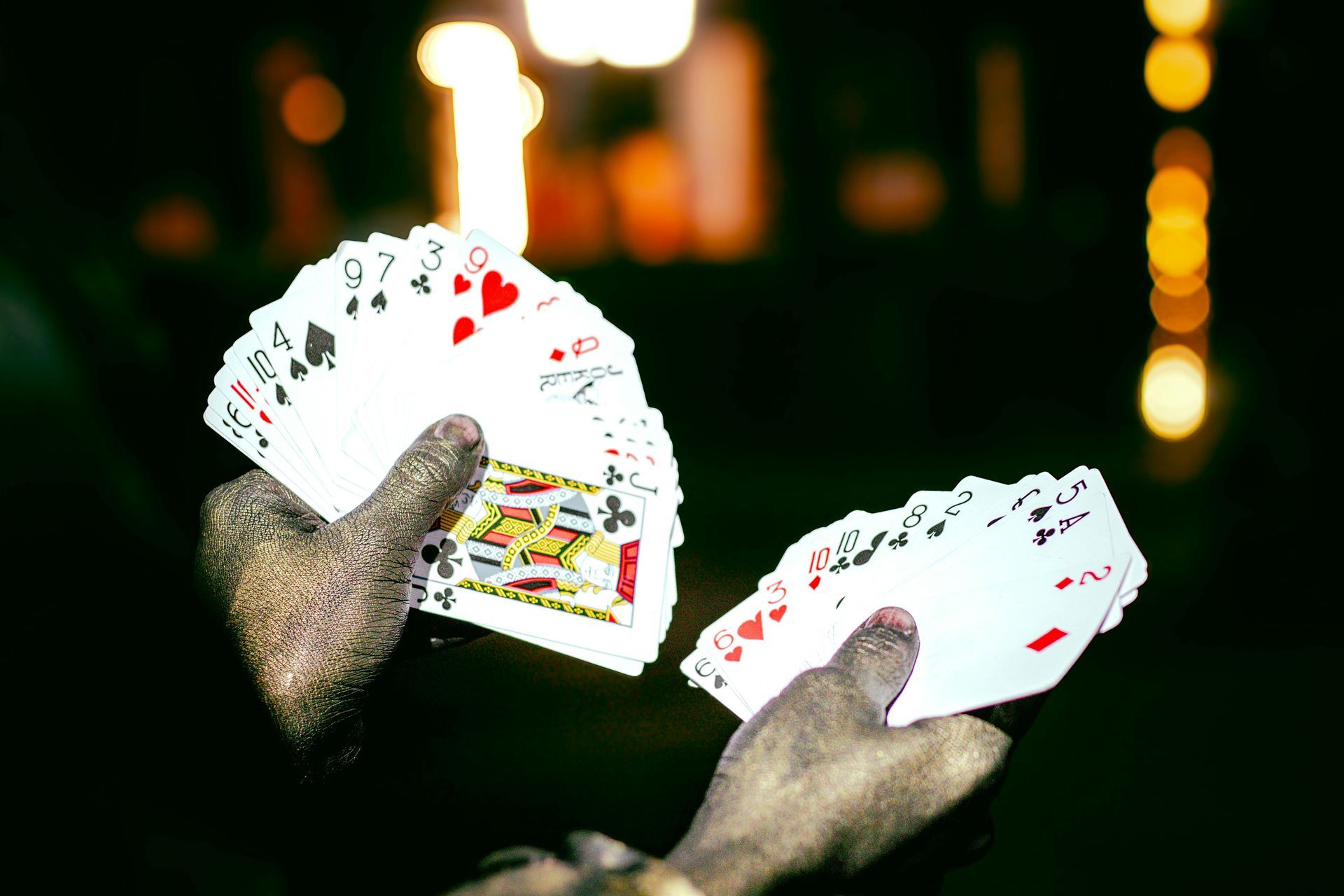 Hands holding fanned playing cards in a dark setting, showing the faces of various suits.