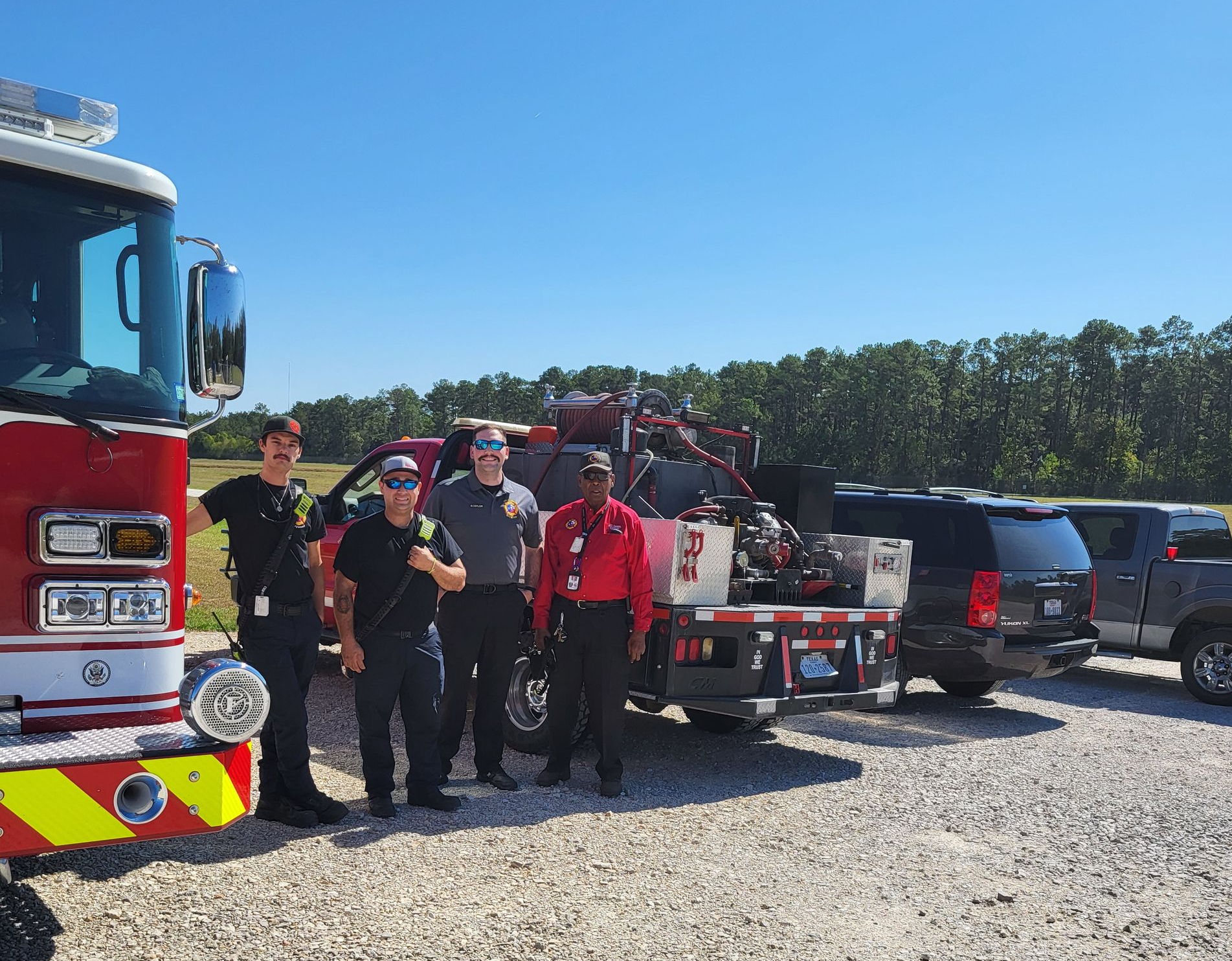 Firefighters standing near a fire truck  holding equipment on a sunny day.