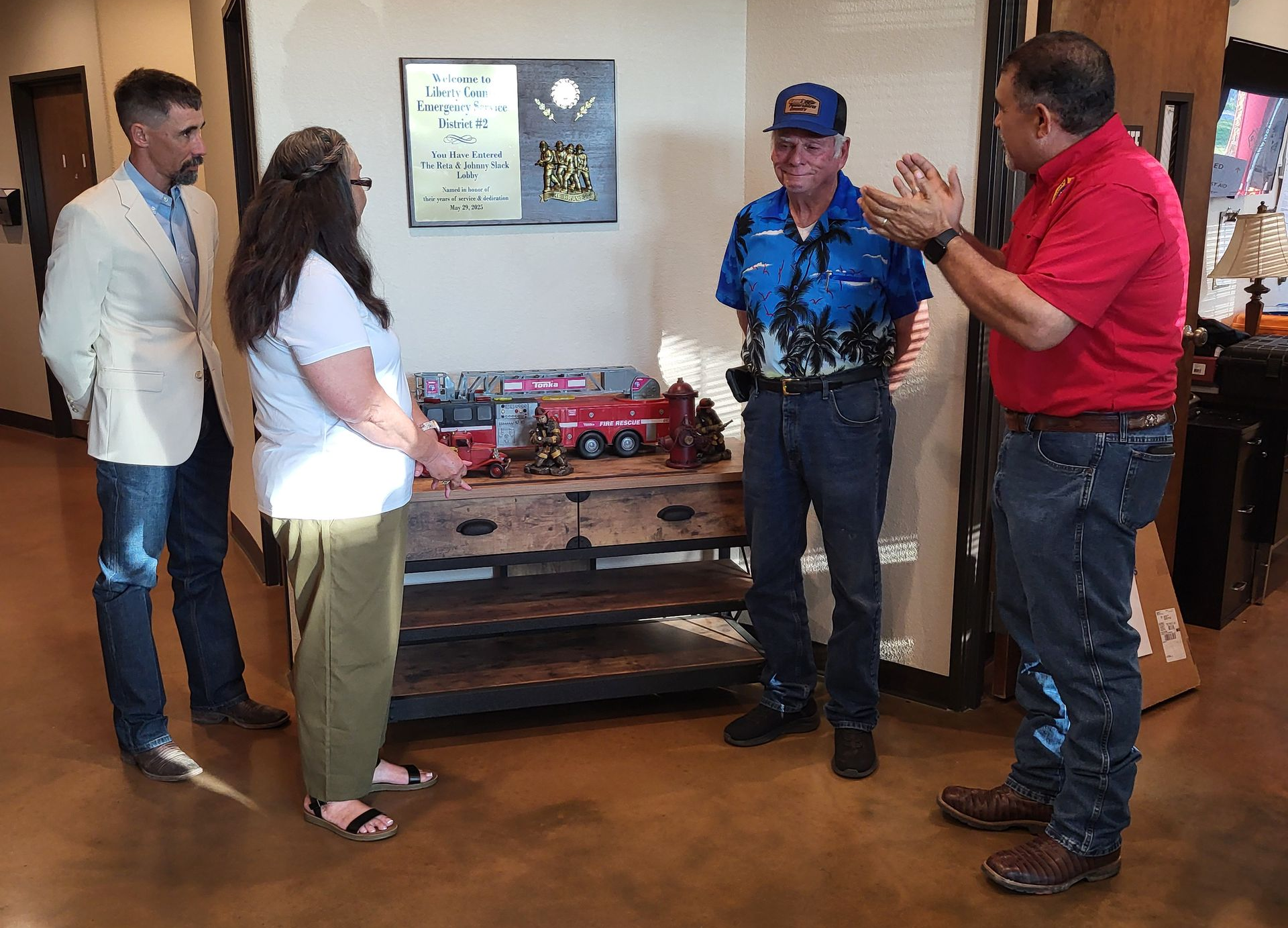 Four people stand near a table with a model truck, inside an office.
