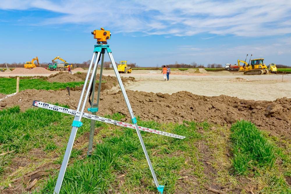 A Tripod is Sitting in the Middle of a Field With a Construction Site — Coastal Surveying Group Pty Ltd in Baringa, QLD
