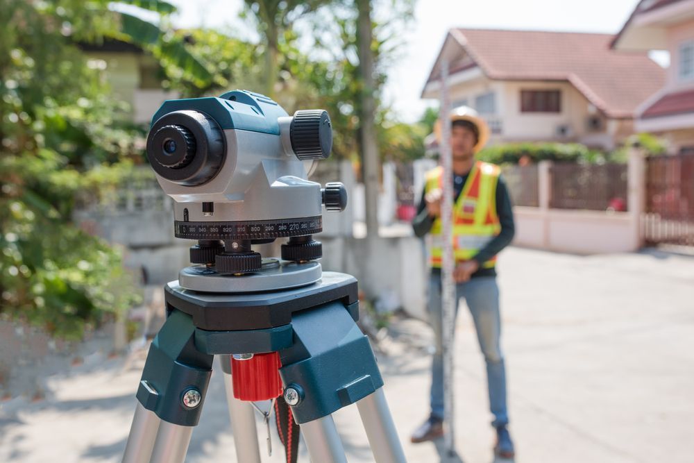 A Man is Standing Next to a Level on a Tripod — Coastal Surveying Group Pty Ltd in Baringa, QLD