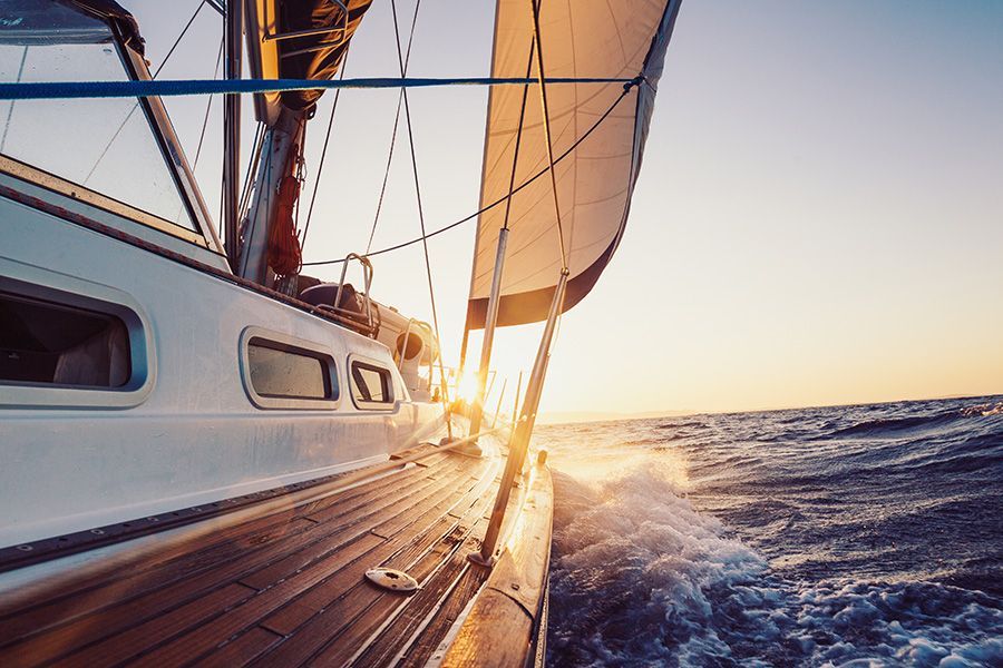 A sailboat is sailing in the ocean at sunset.