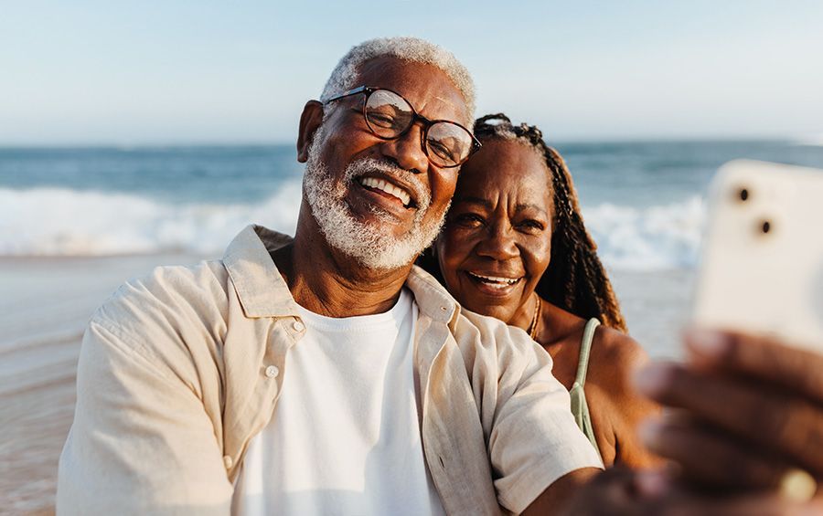 An elderly couple is taking a selfie on the beach.