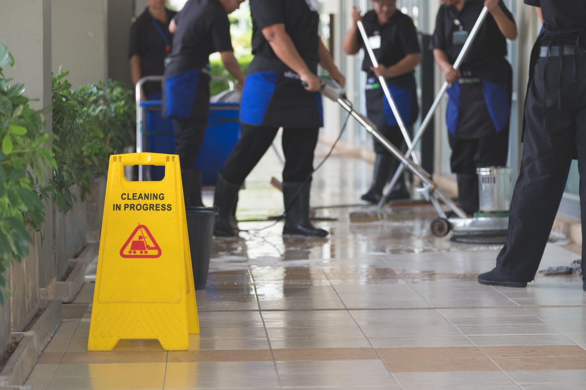 A group of men are cleaning a tiled floor next to a yellow caution sign.