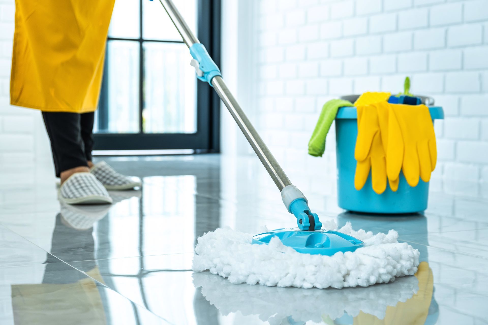 A person is cleaning the floor with a mop and gloves.