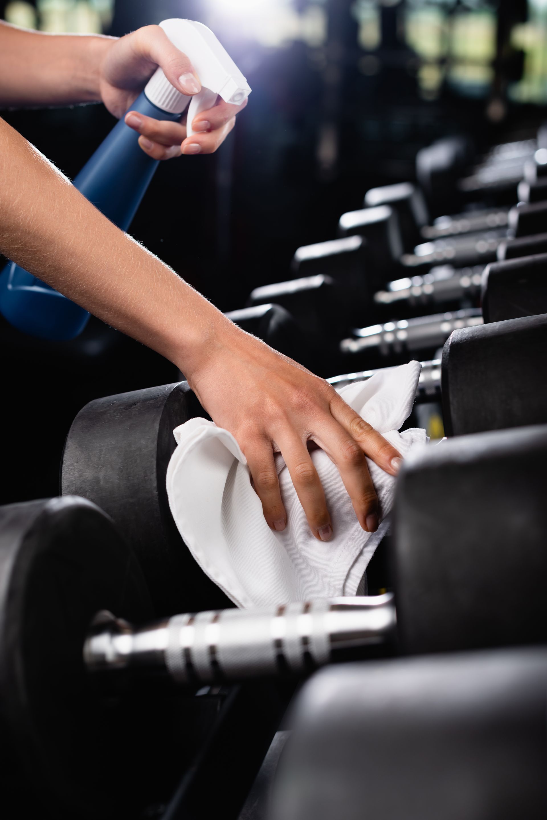 A person is cleaning a row of dumbbells in a gym.