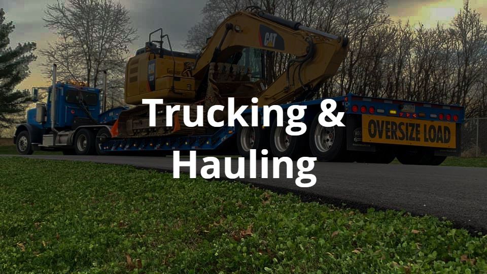 A truck from R. Work Excavating & Trucking is hauling a bulldozer down a road.