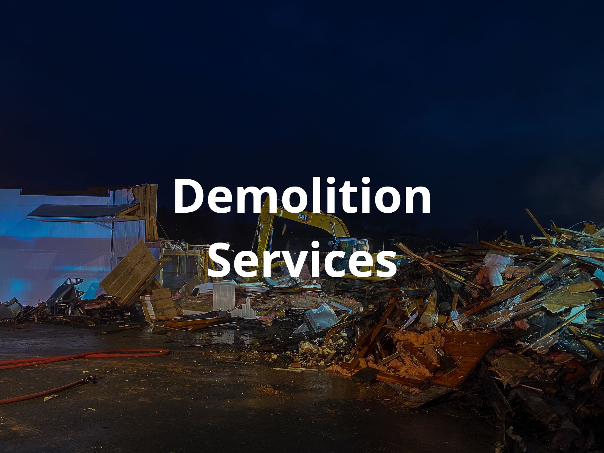 A picture of a building being demolished at night by an excavator from R. Work Excavating & Trucking with the words `` demolition services '' written above it.