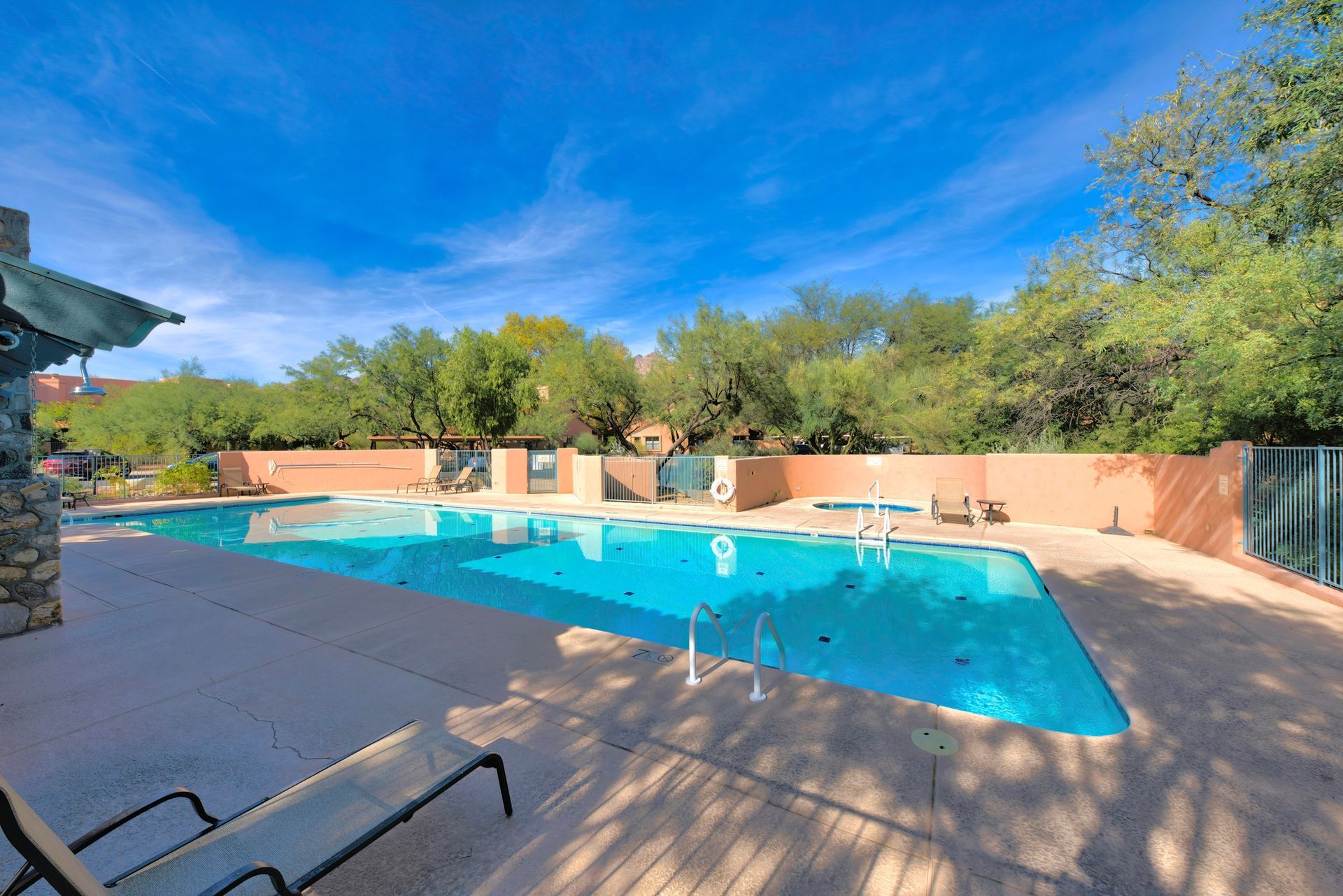 A large swimming pool surrounded by trees and chairs on a sunny day.