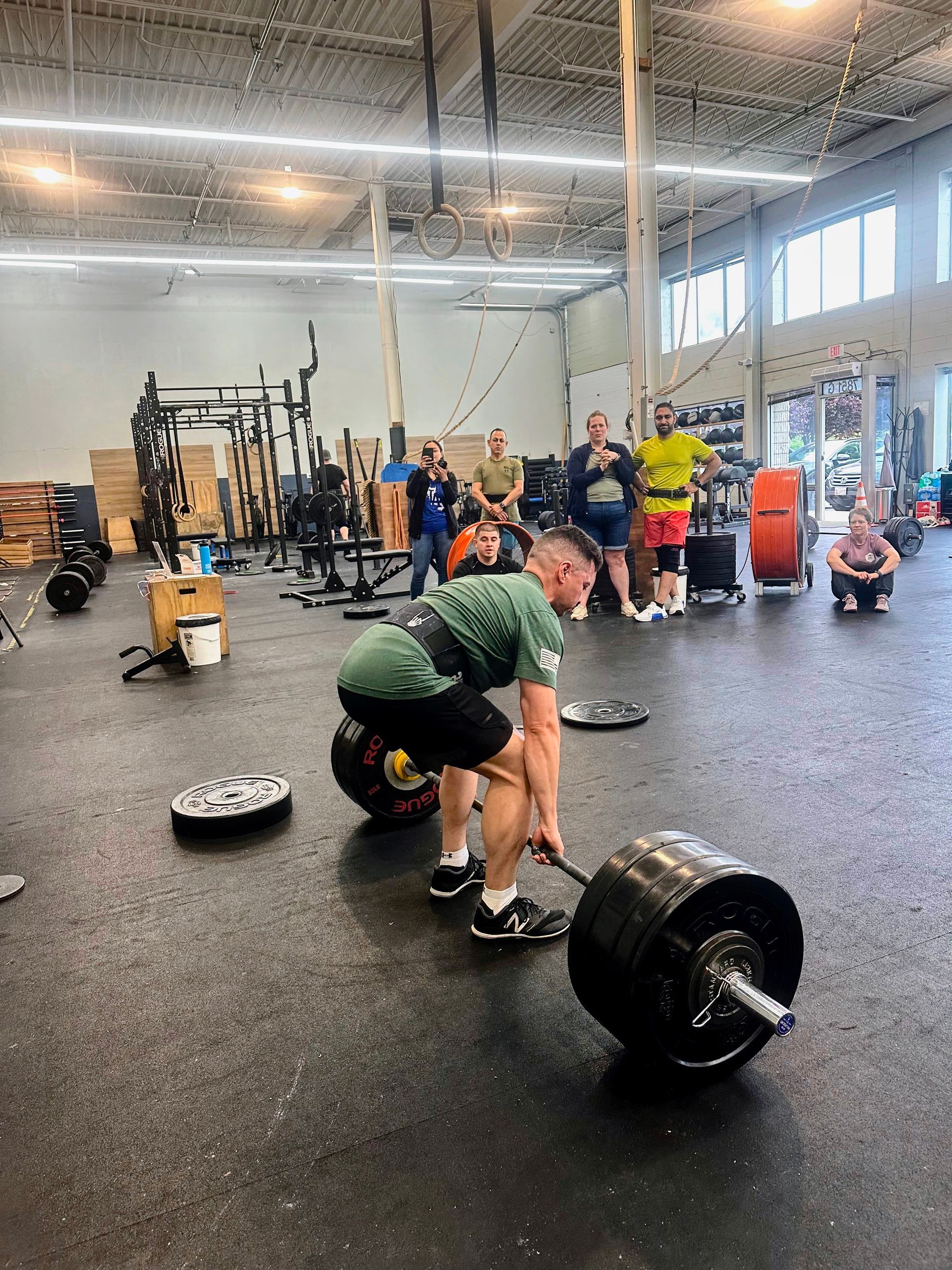 A man is squatting down to lift a barbell in a gym.