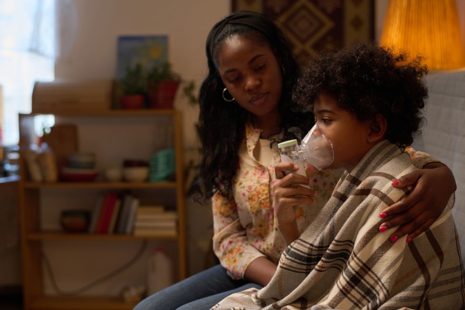 A woman is sitting on a couch with a child wearing an oxygen mask.