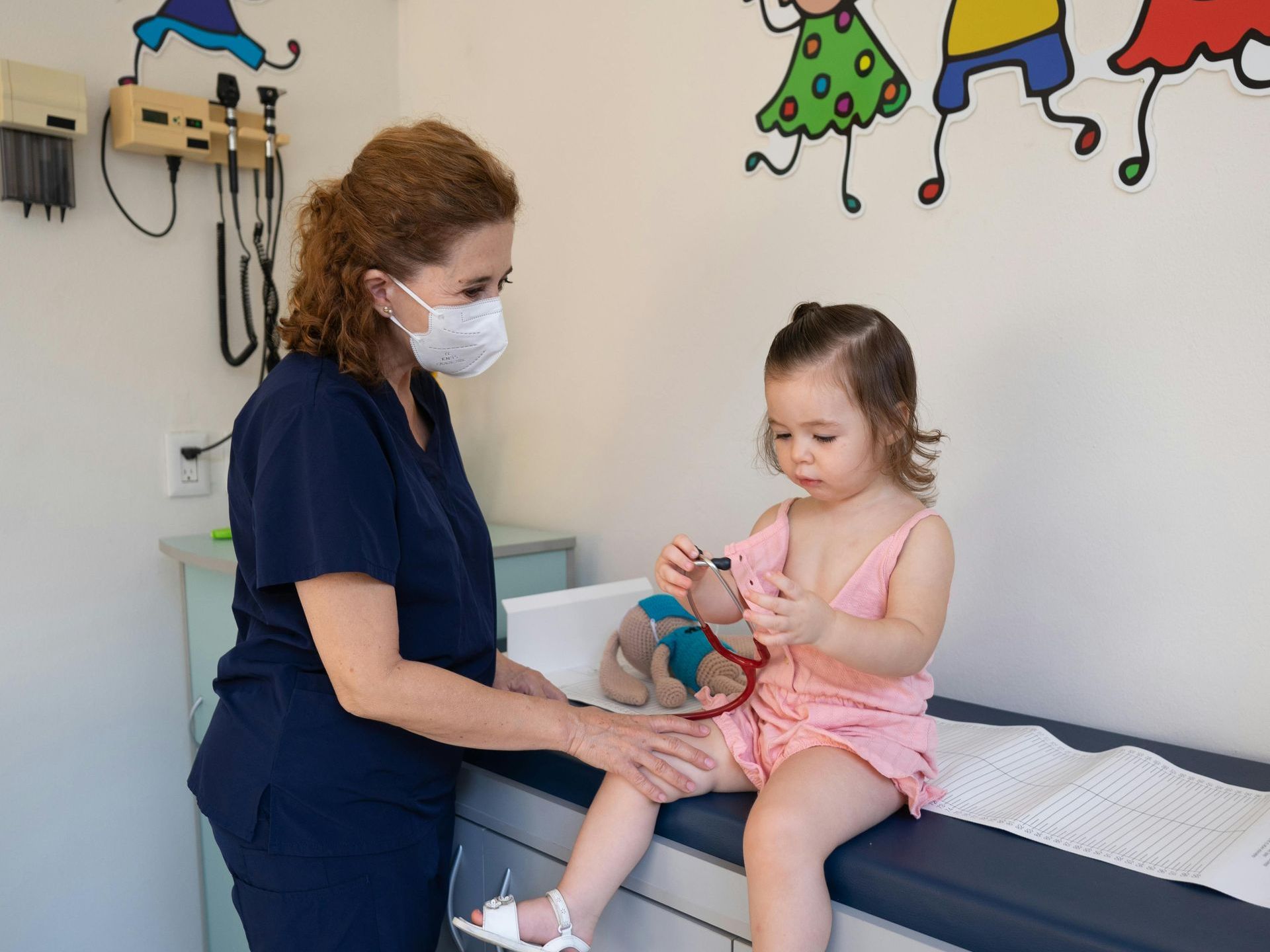 A pediatrician wearing a mask is examining a little girl.