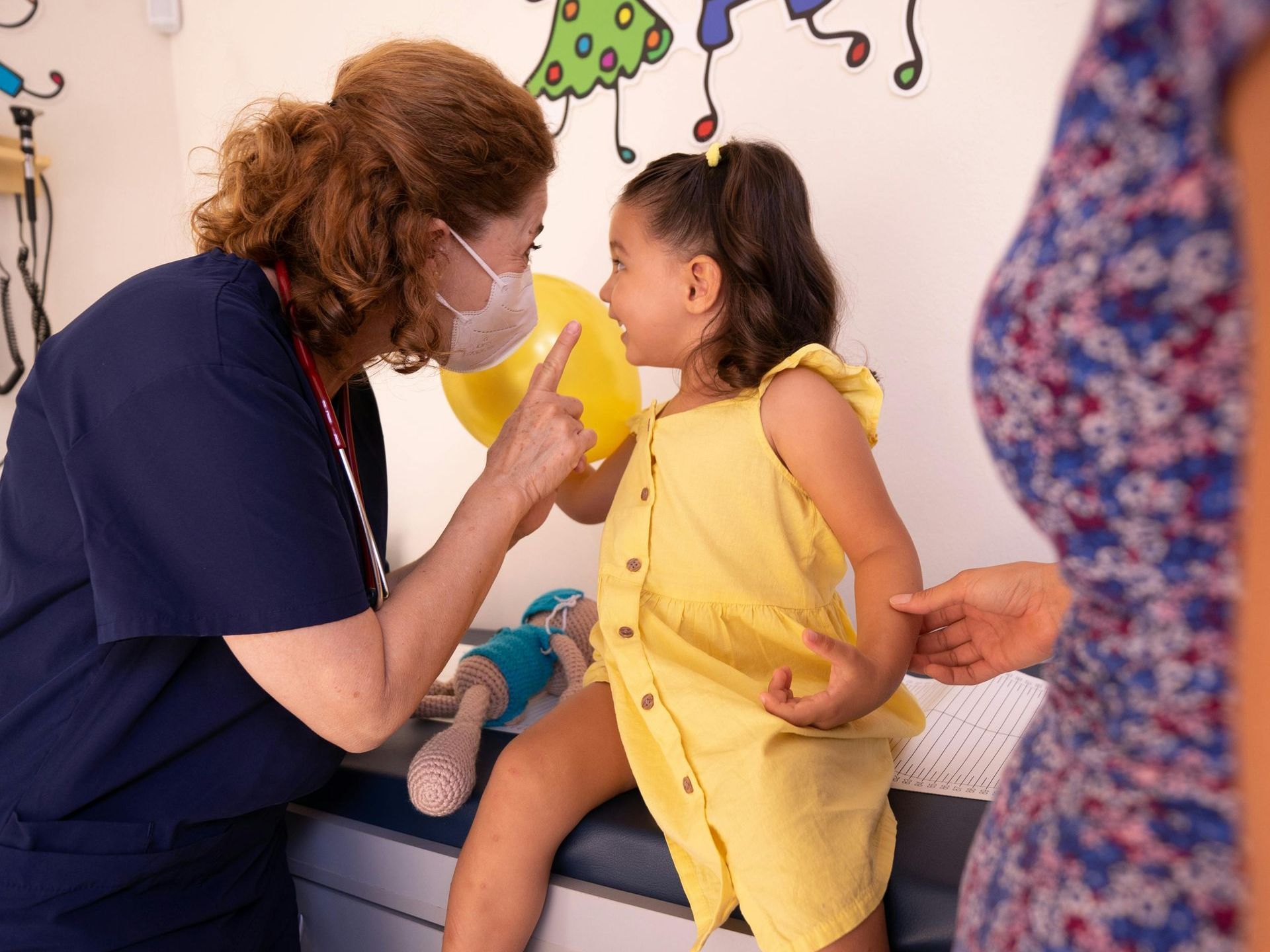 A pediatrician is talking to a little girl in a yellow dress.