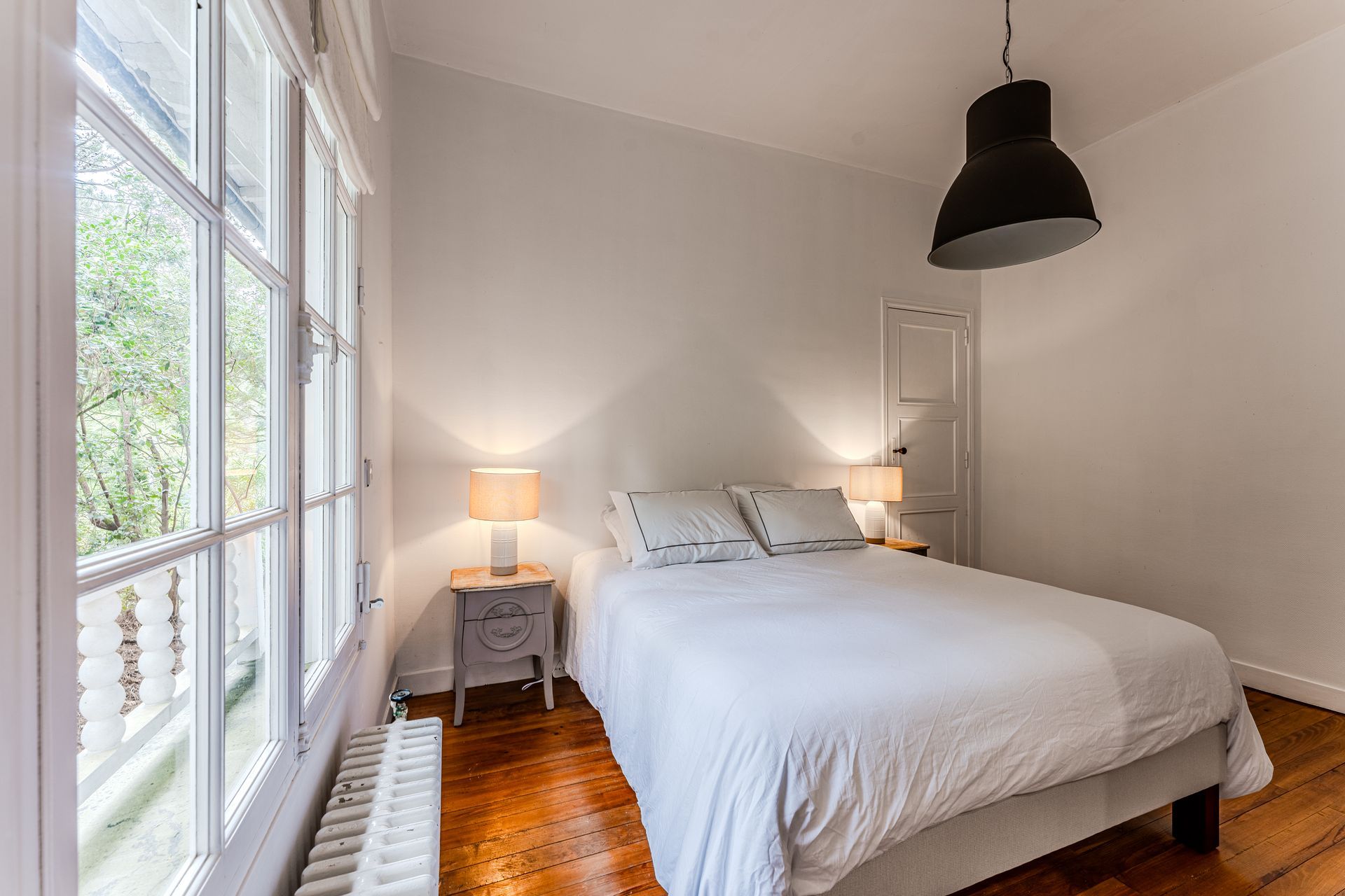 Une chambre avec un lit, une table de chevet, une lampe et une fenêtre.