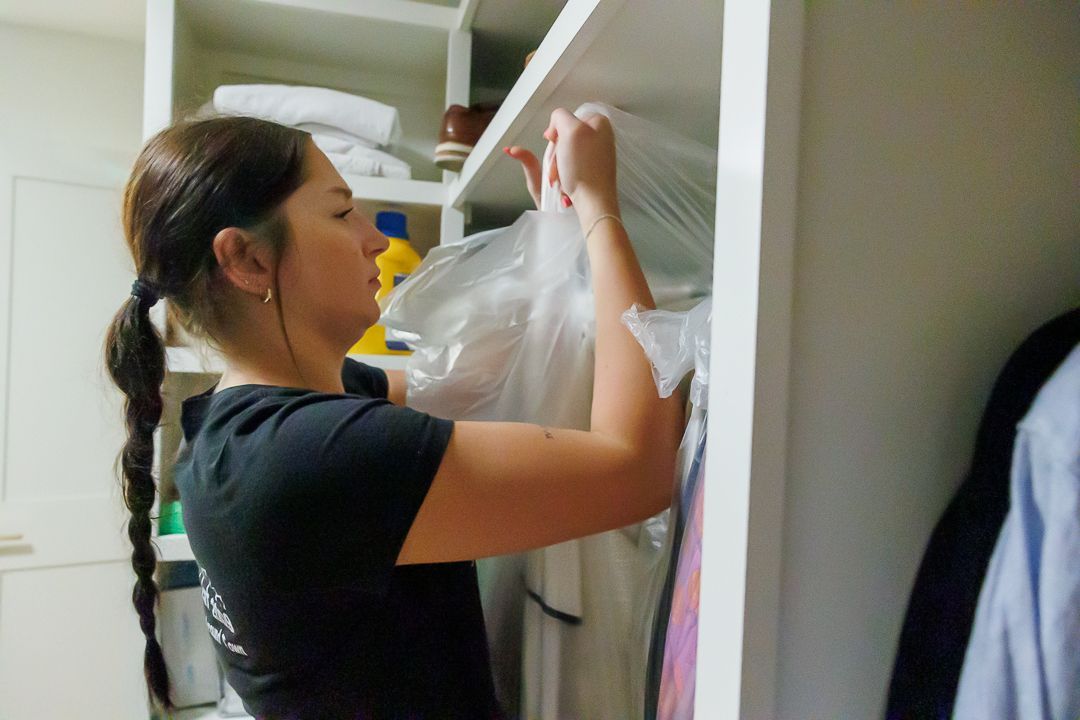 Woman in black shirt, putting clothes in a white closet.