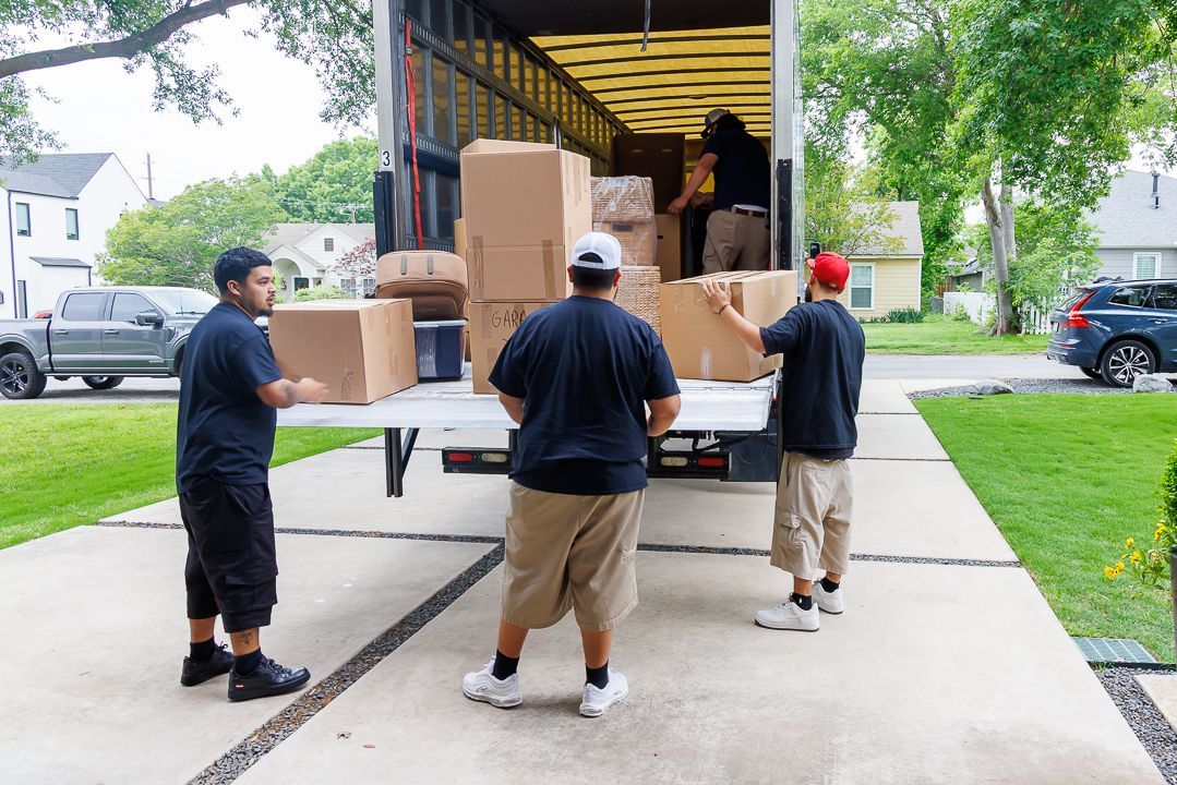 Movers unloading boxes from a truck on a driveway, loading into the truck.