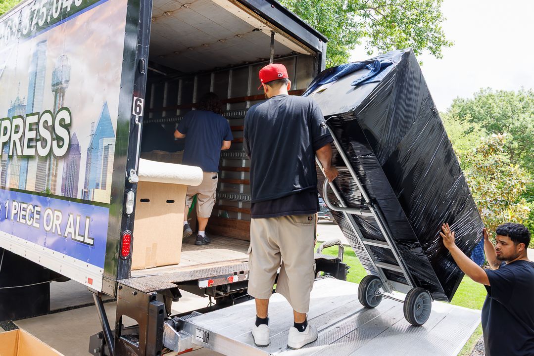 Movers loading a large, wrapped sofa onto a truck using a dolly.