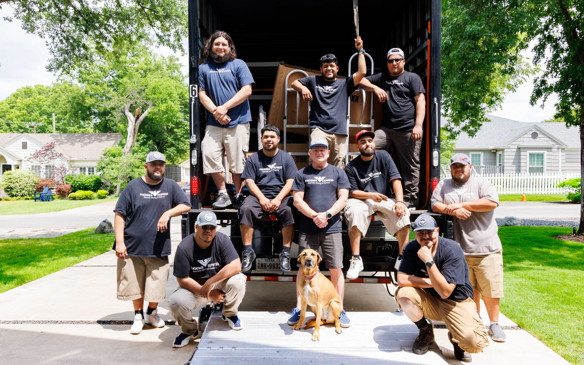 Moving crew poses with a dog by their truck on a residential driveway.
