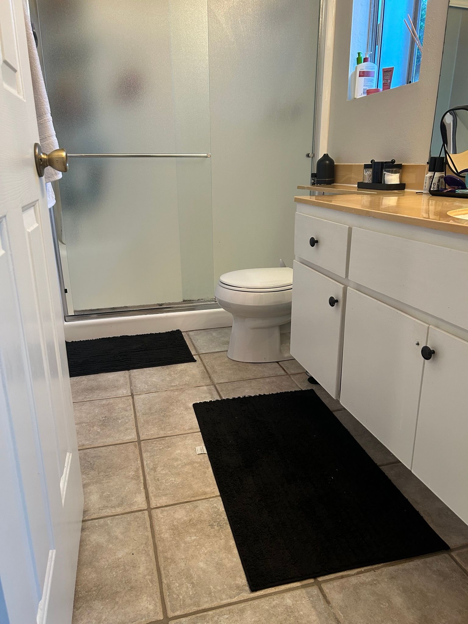 Bathroom with white cabinets, toilet, shower, and black bath mats.