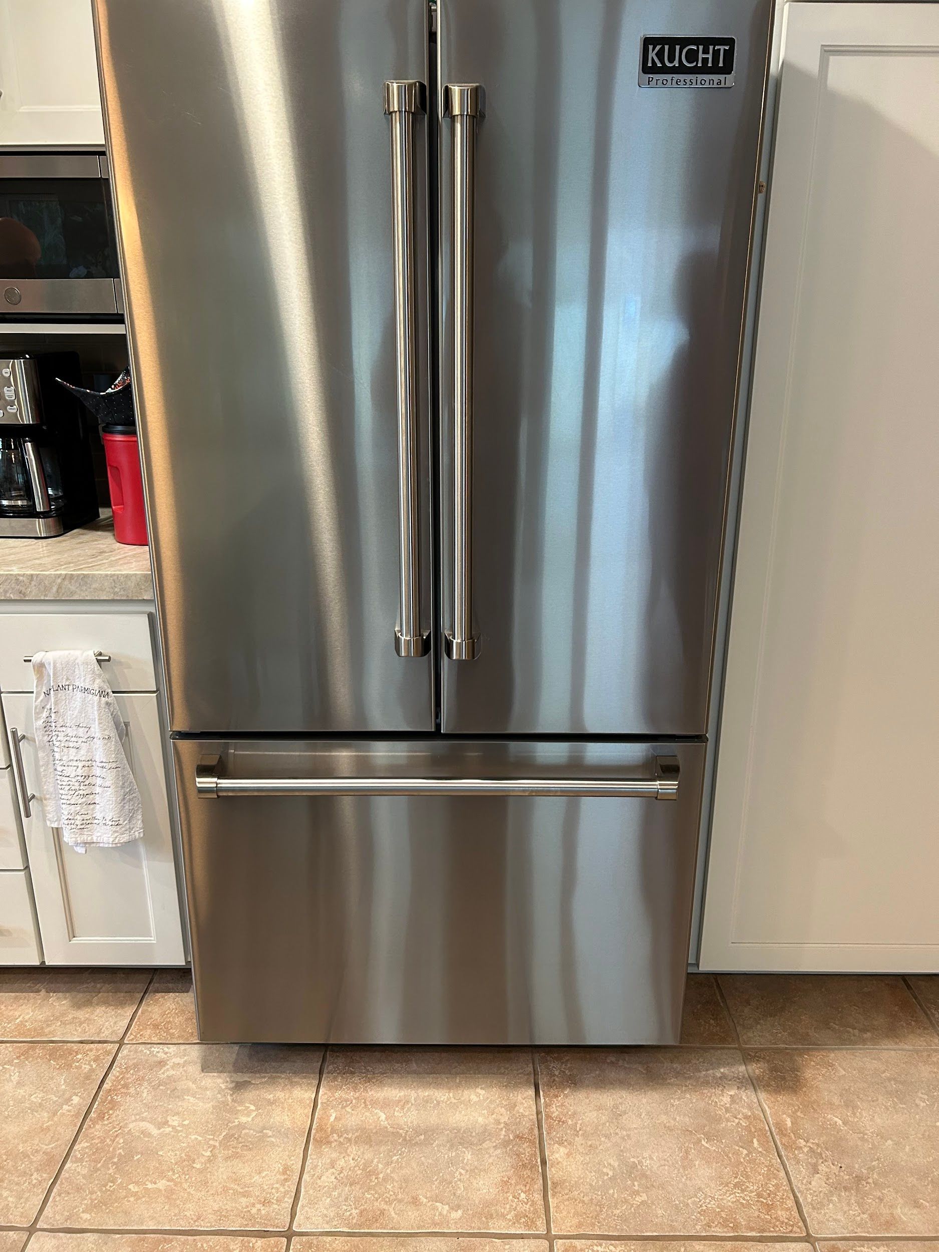 Stainless steel, three-door refrigerator with chrome handles in a kitchen setting.