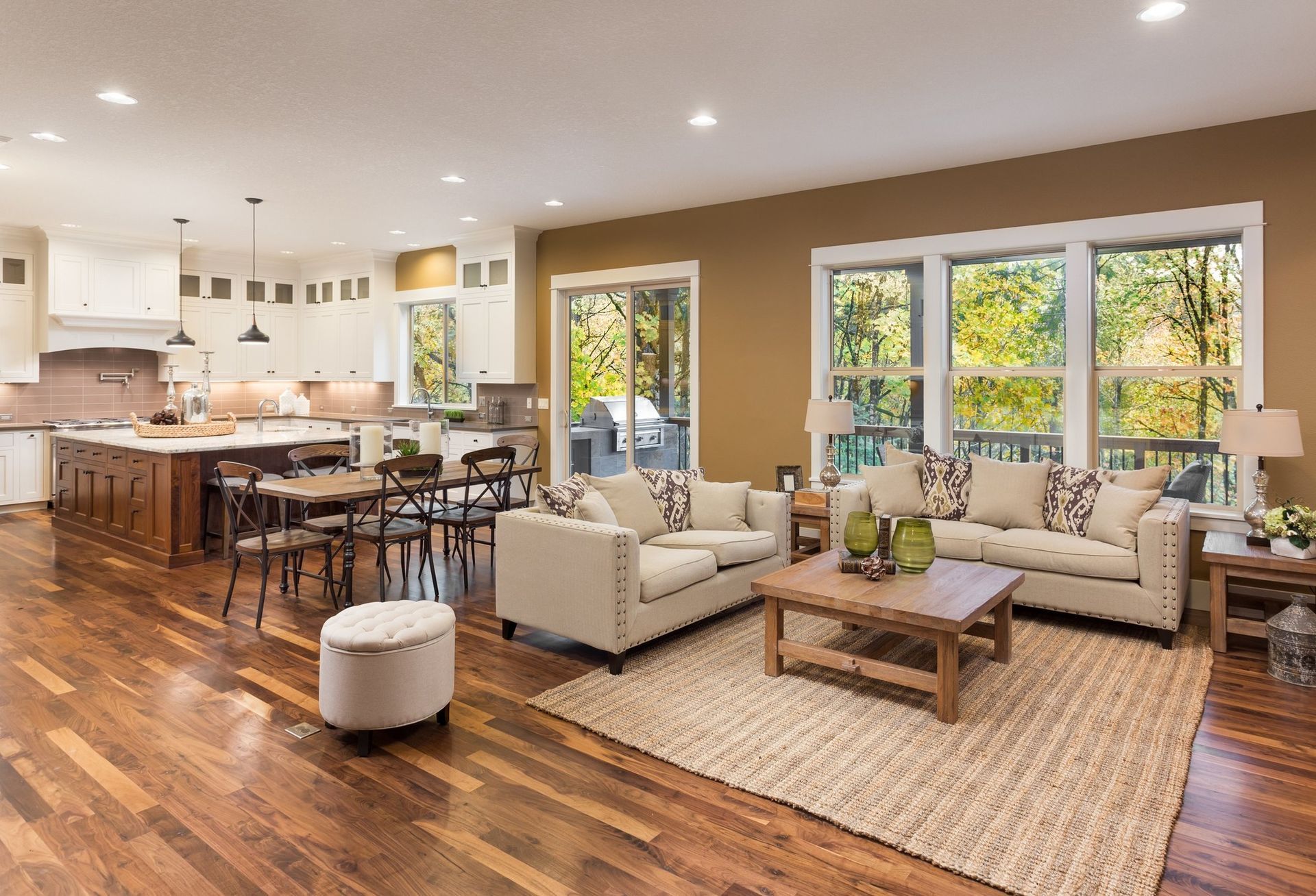 Open-concept living room with kitchen, dining, and seating areas; hardwood floors, beige furniture.