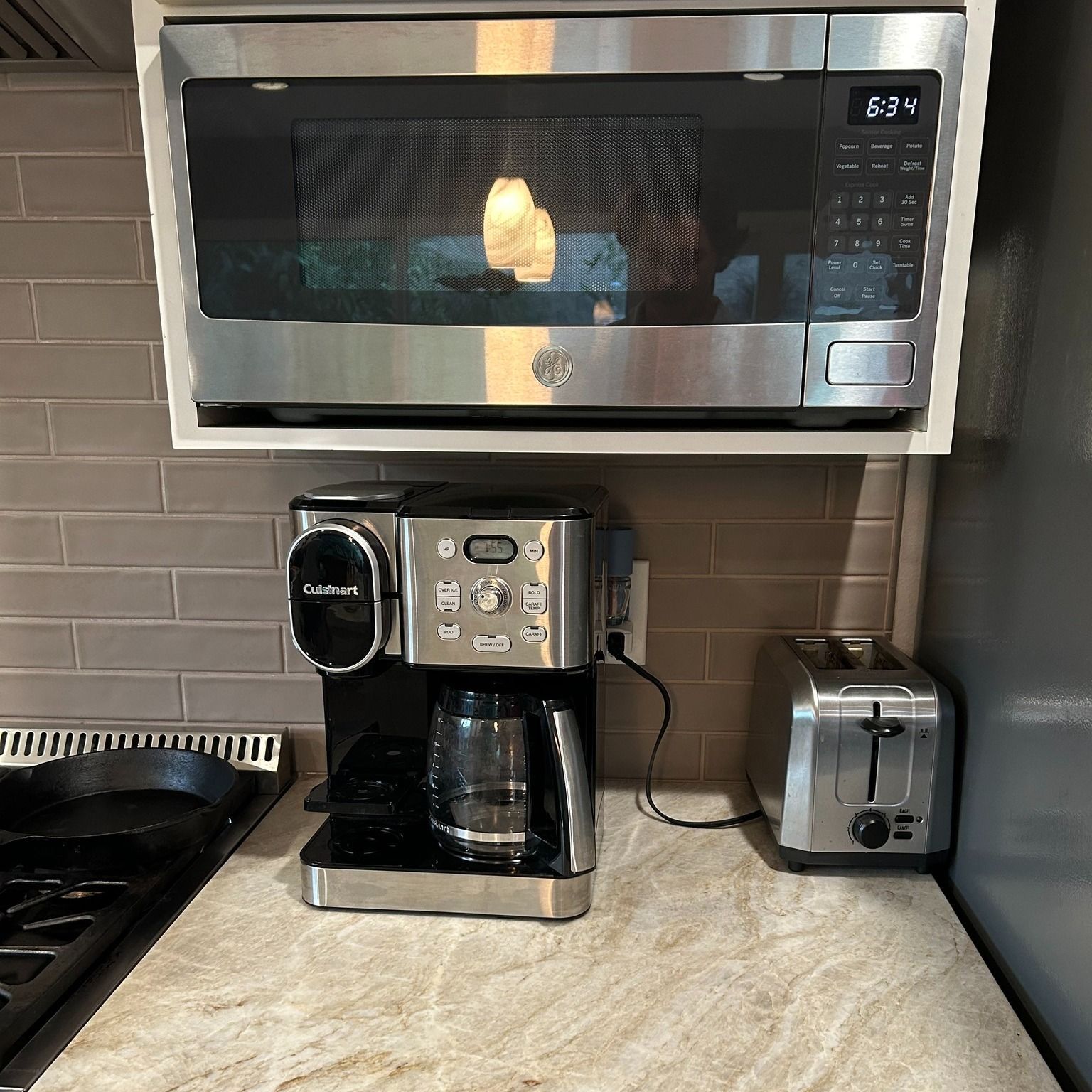 Microwave above coffee maker and toaster on a kitchen counter with backsplash.