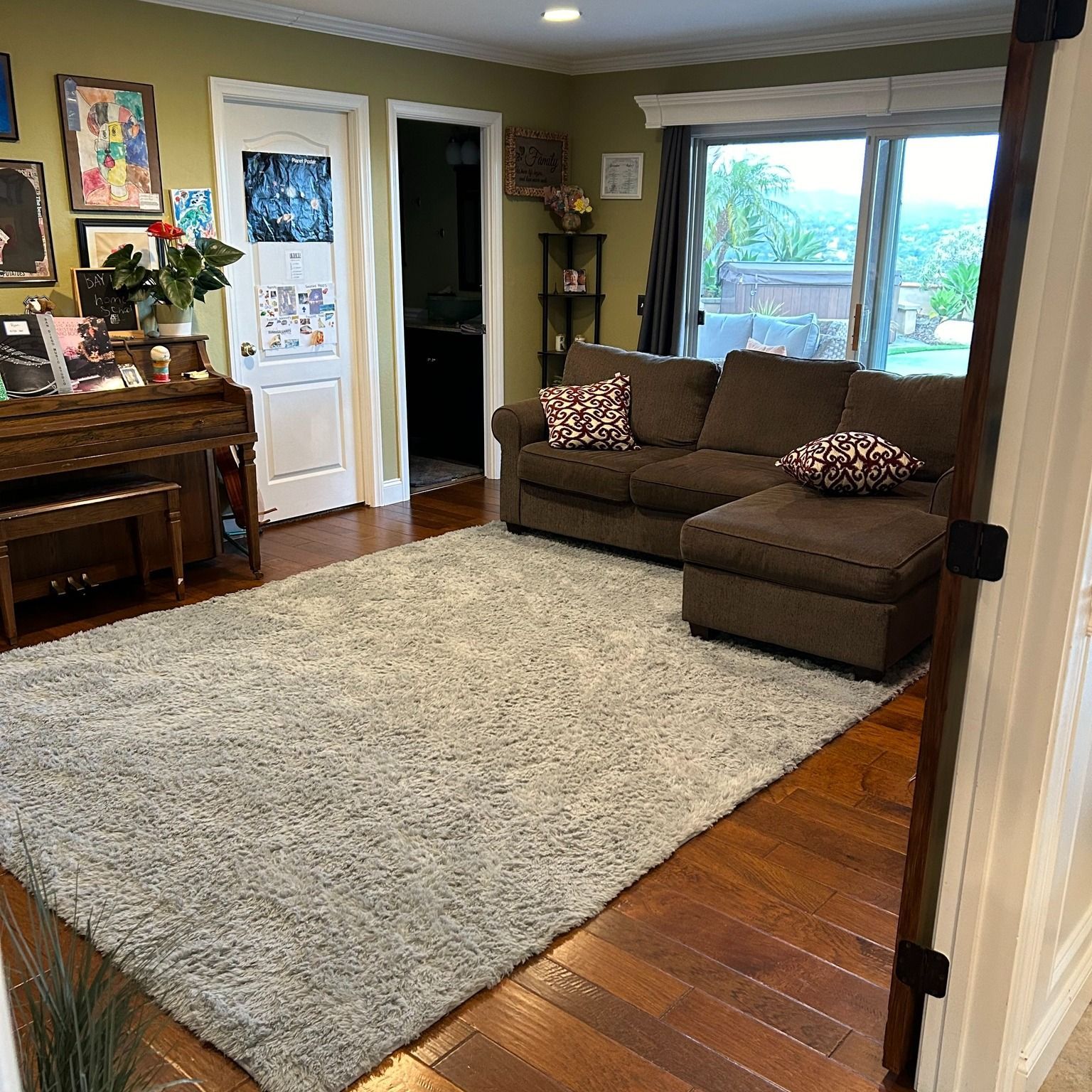 Cozy living room with a brown sectional, a shaggy rug, and a piano near a door.