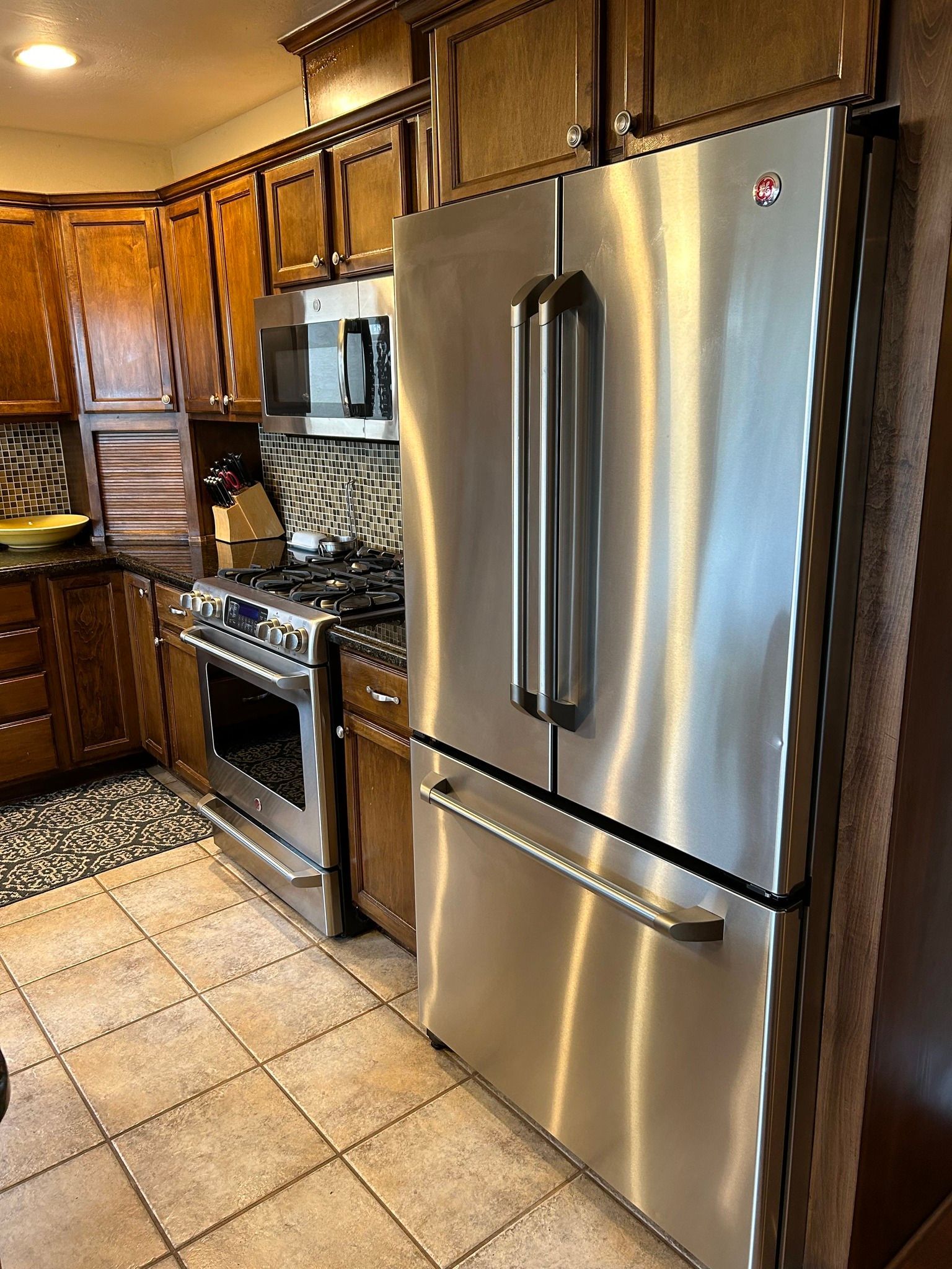 A stainless steel refrigerator next to a stove in a kitchen with wooden cabinets and a patterned backsplash.