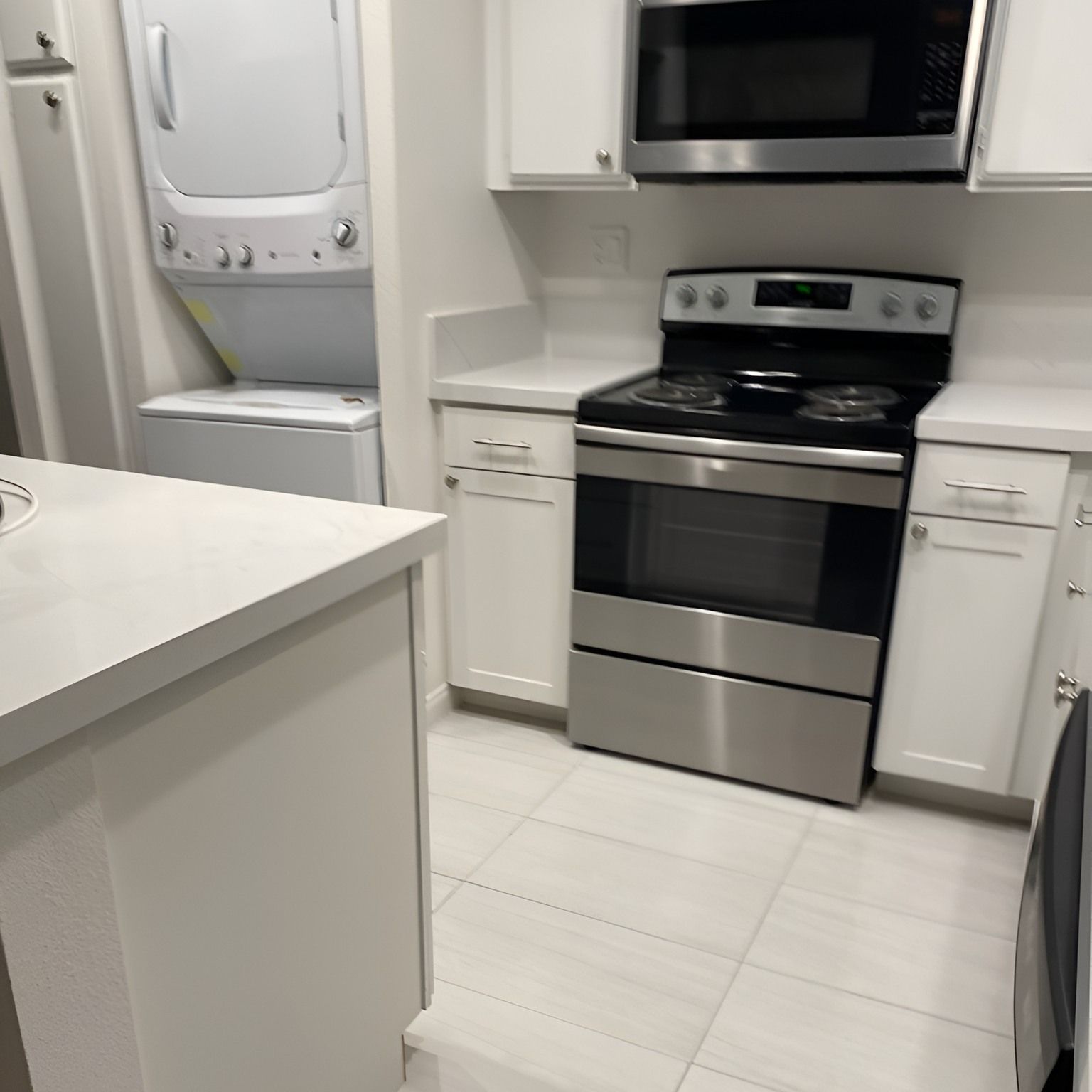 White kitchen with stainless steel appliances, white cabinets, and stacked washer and dryer.