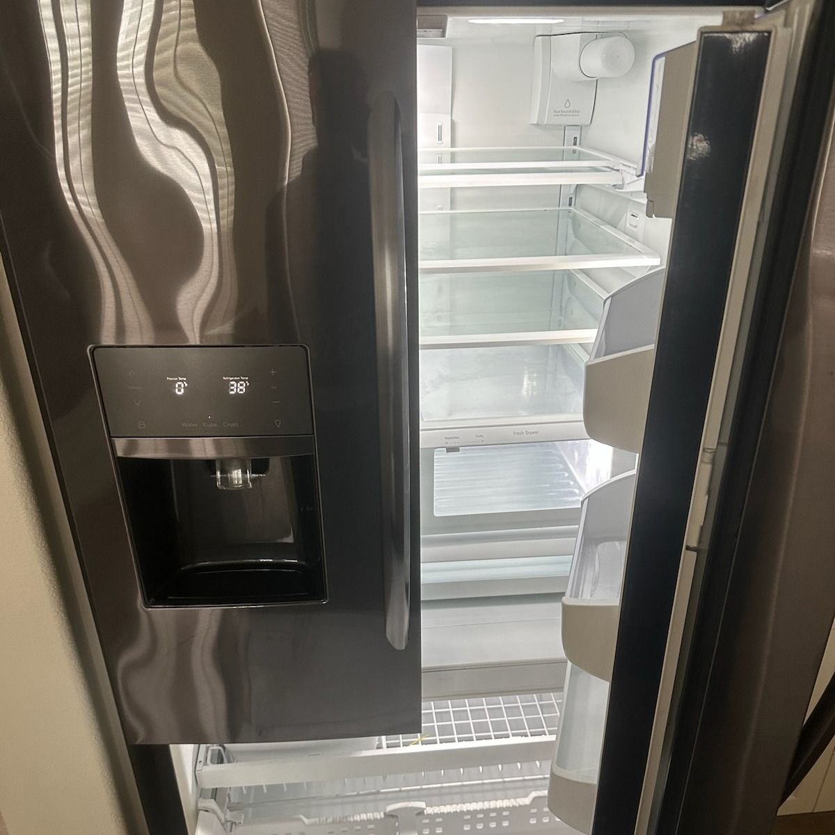A dark gray, open refrigerator. Inside, the shelves are clear, and the door has a water dispenser.