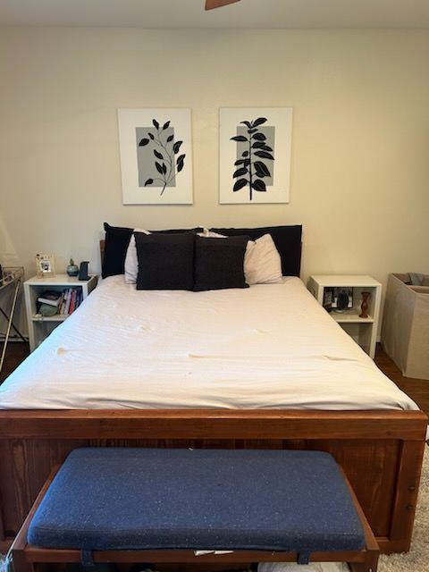 Bedroom with wooden bed, two framed plant art pieces, nightstands, and a blue bench.