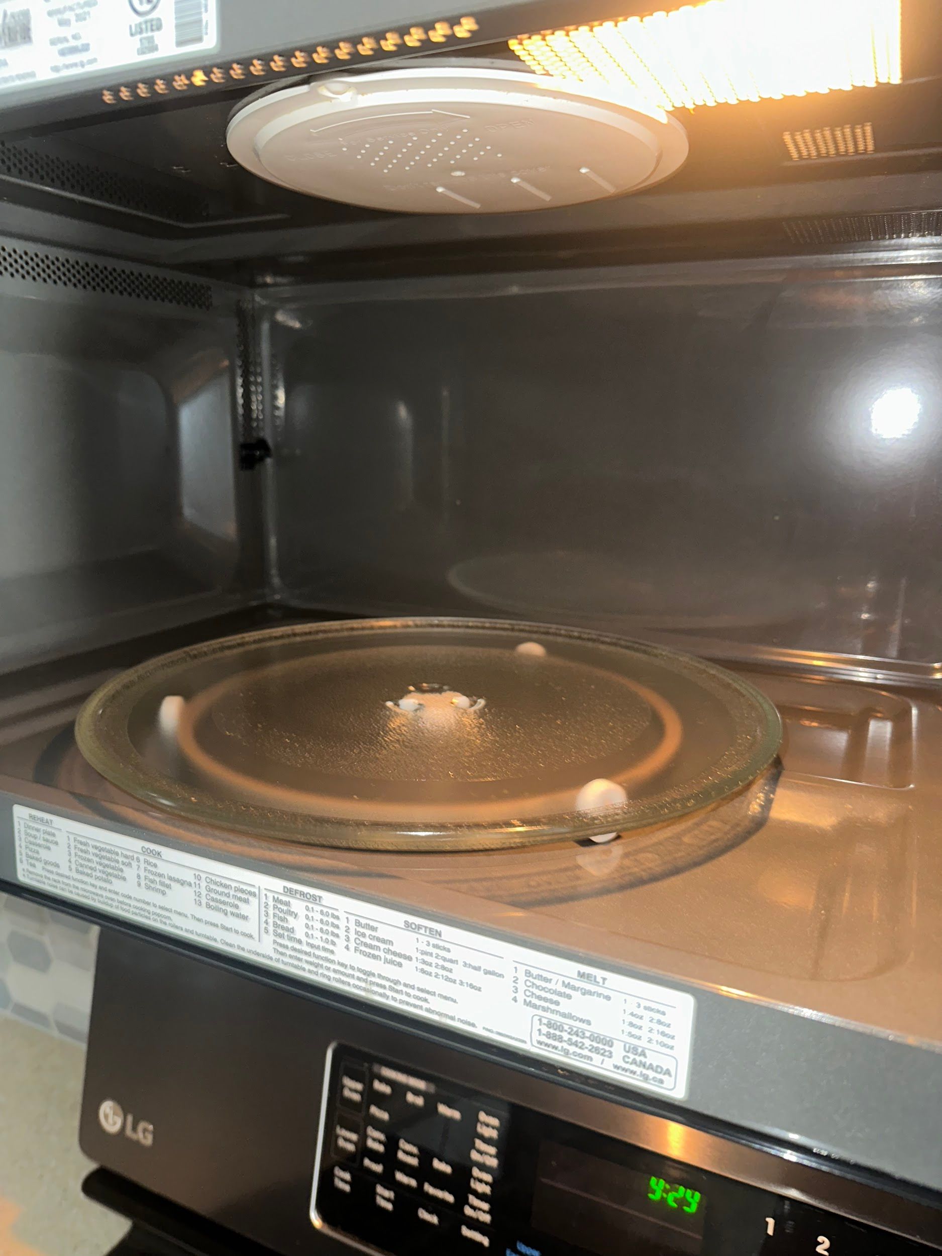 Interior view of a microwave oven with a glass plate and top cover, lit from above.