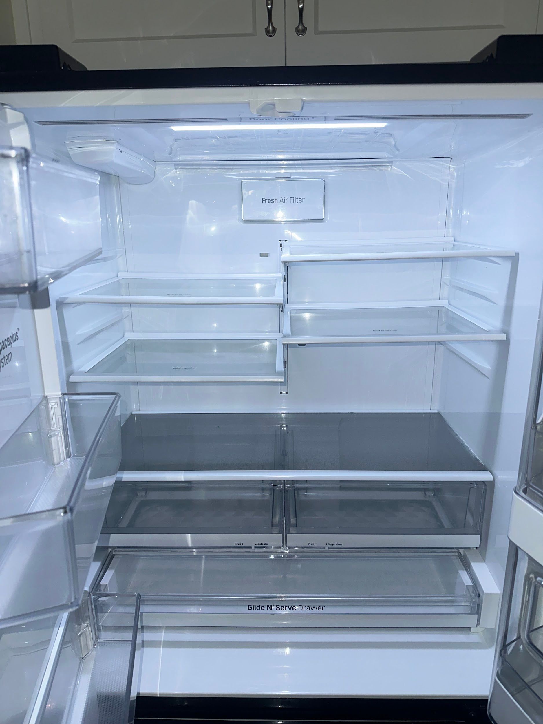 Empty, open refrigerator interior with glass shelves and drawers, lit by overhead light.
