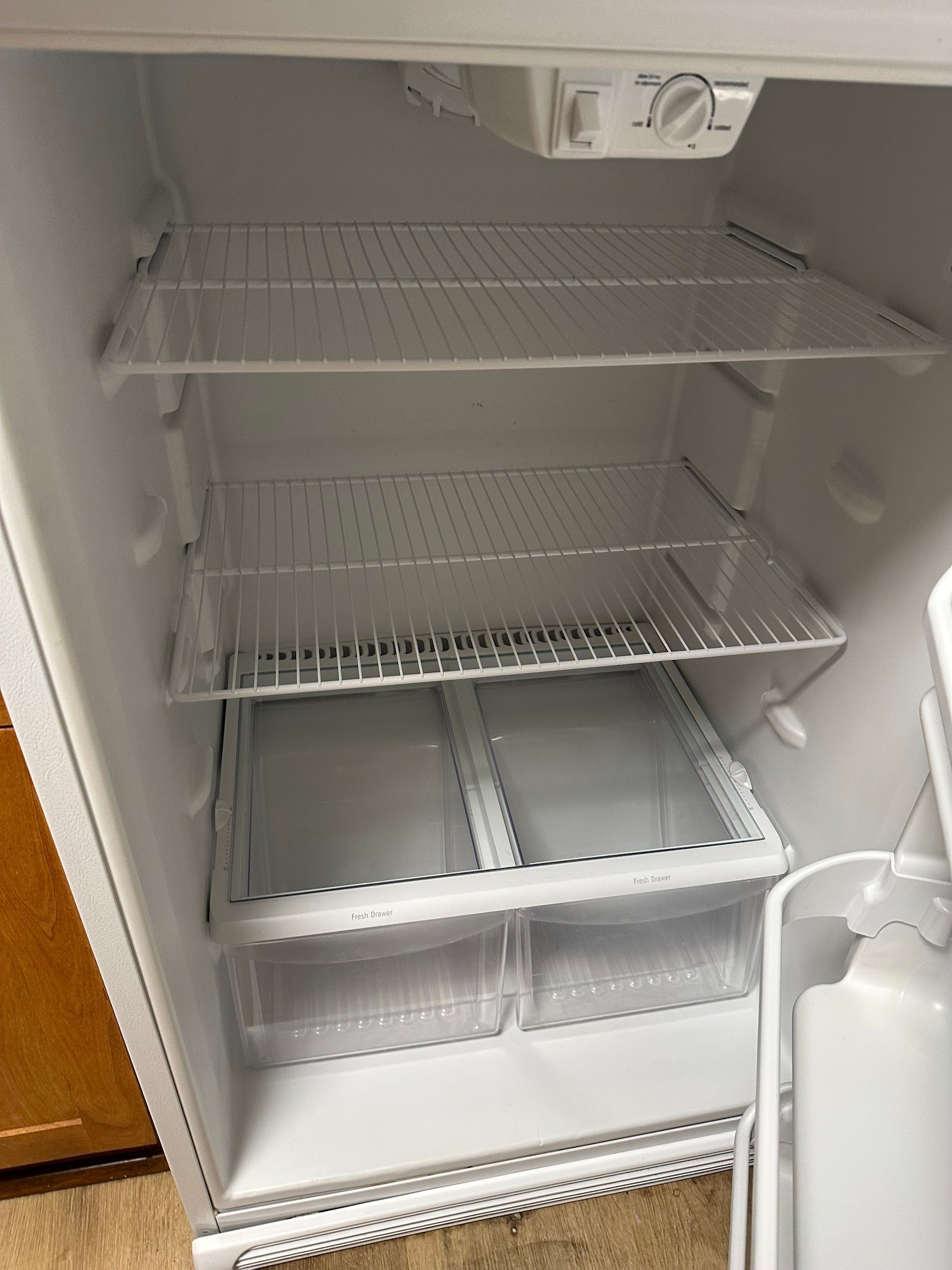 An empty white refrigerator interior with wire shelves and two bottom drawers.