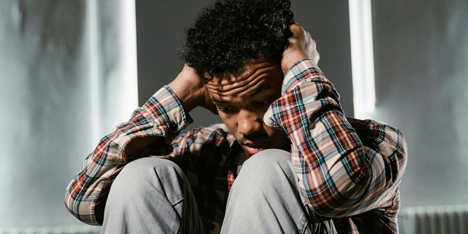 Man looking vulnerable and scared, legs pulled up, head in his hands.