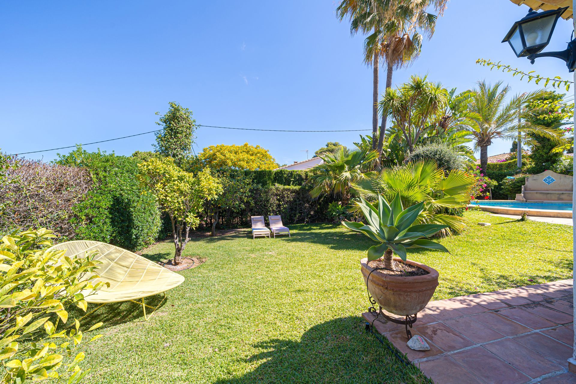 Un exuberante jardín verde con una silla amarilla al fondo de Villa Fave en Xabia, El Tosalet