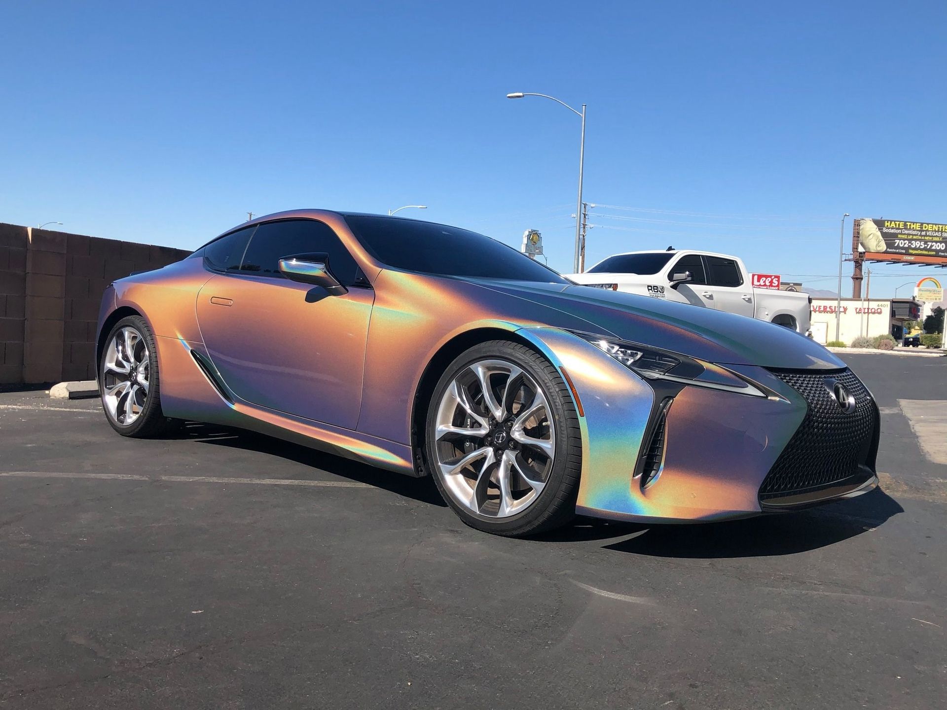 Iridescent sports coupe parked on asphalt under a clear blue sky.