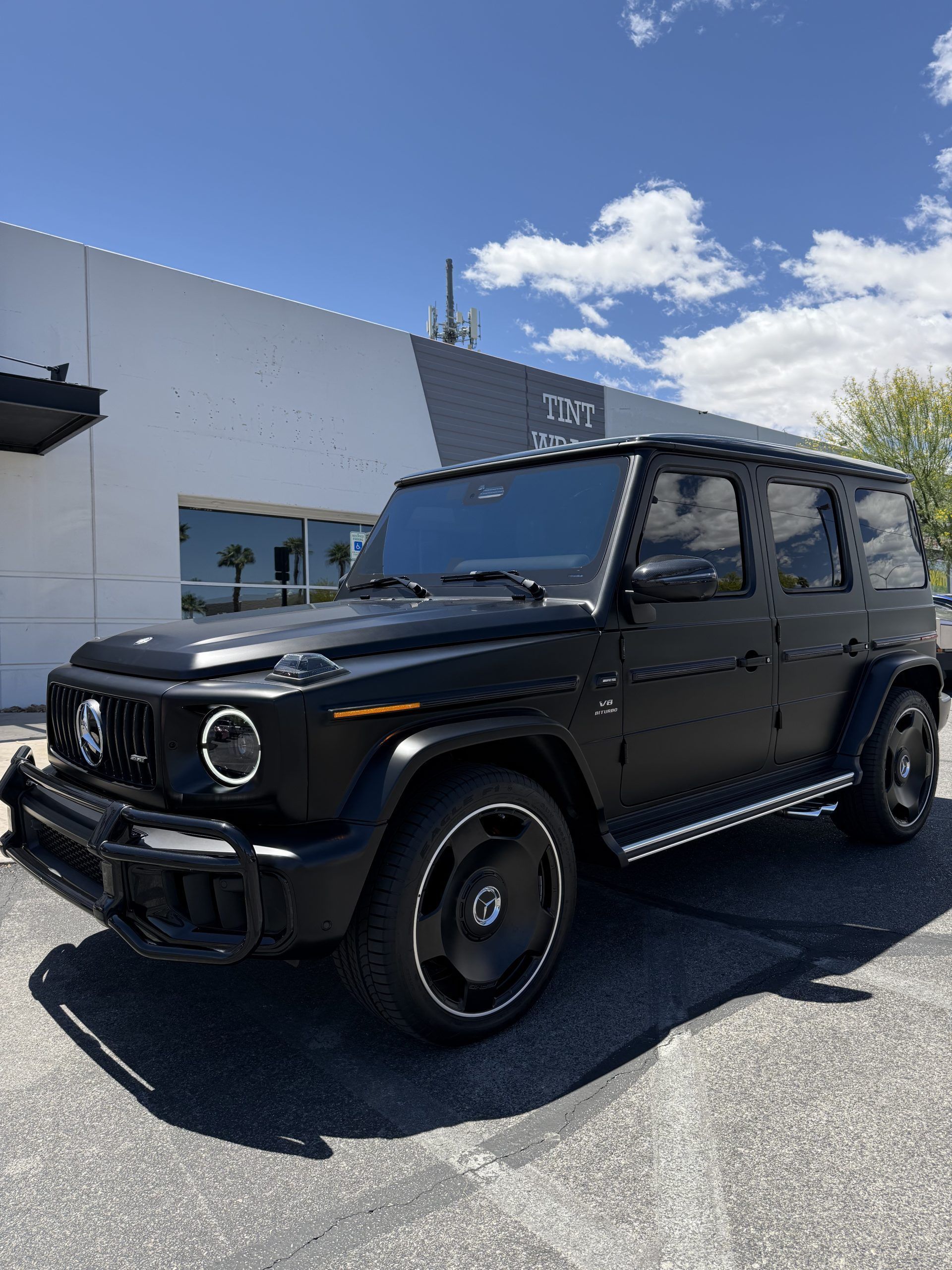 Black Mercedes-Benz G-Class SUV parked outside a dealership under a blue sky